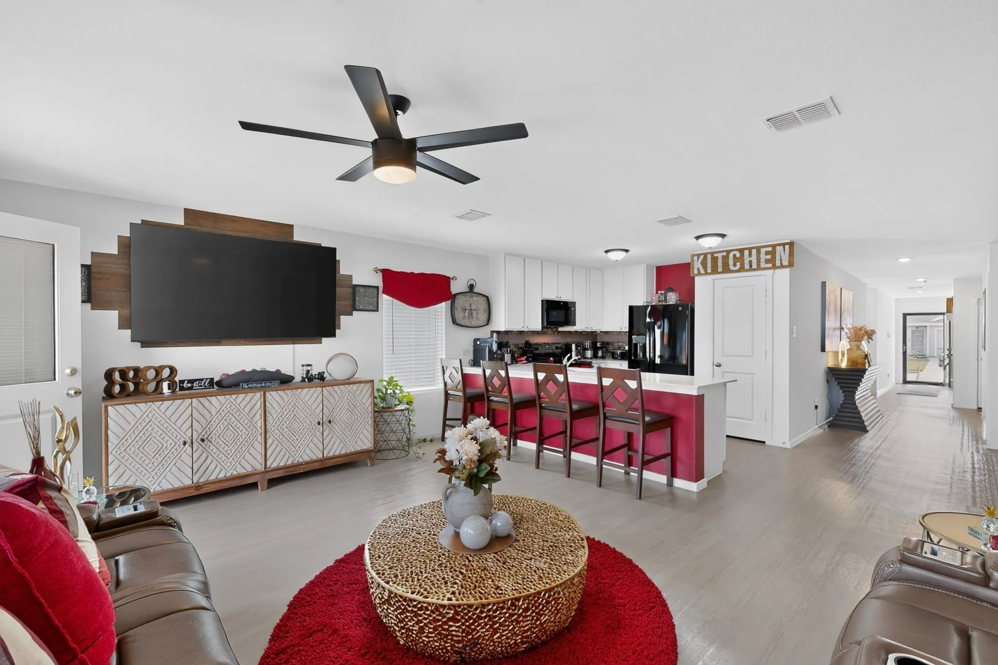 Open-concept living area with wood-finish flooring, a contemporary ceiling fan, kitchen island with seating, white cabinetry, and black appliances