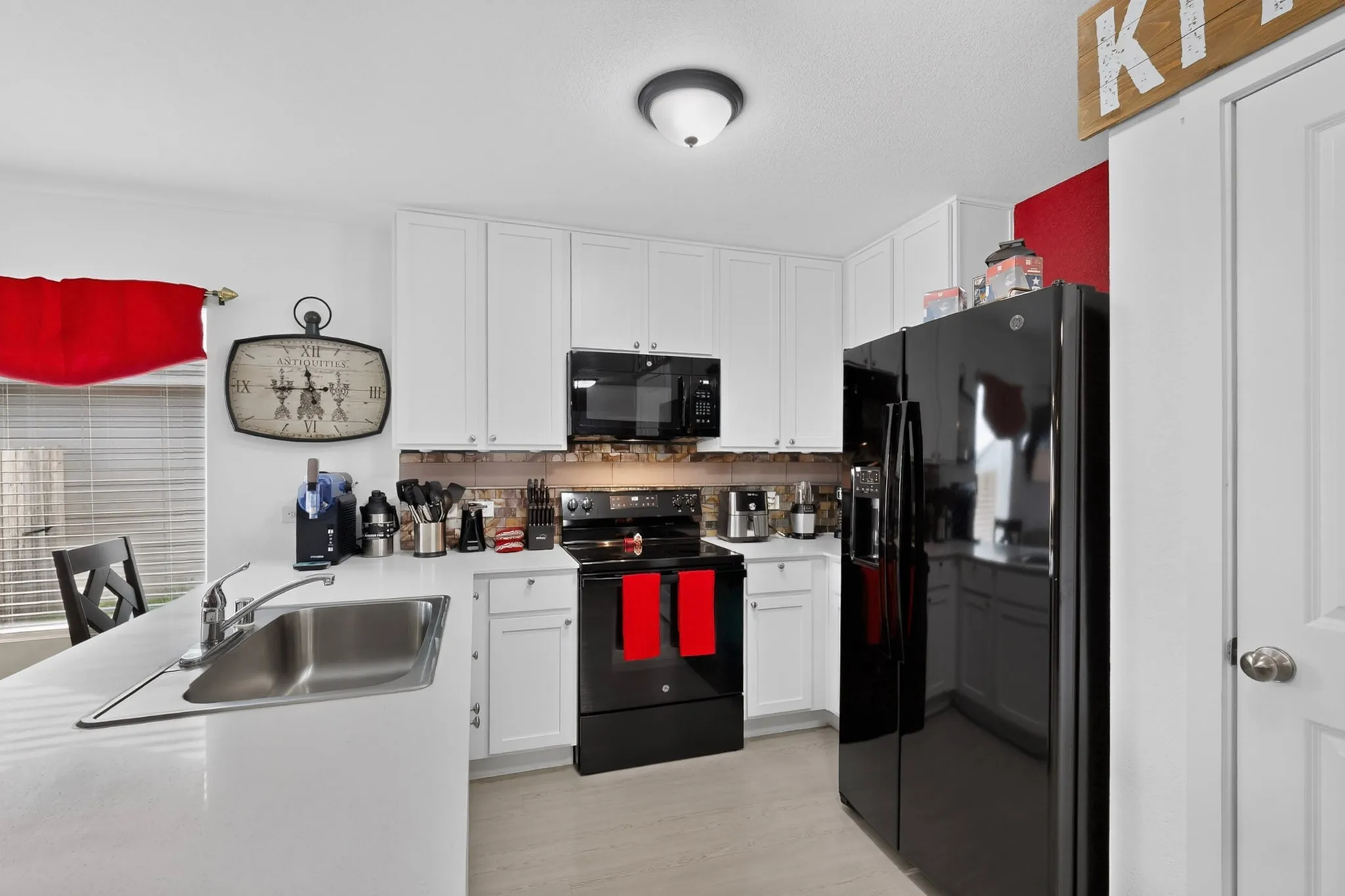 White cabinetry with brushed nickel hardware, stainless steel sink, black appliances, and a tiled backsplash