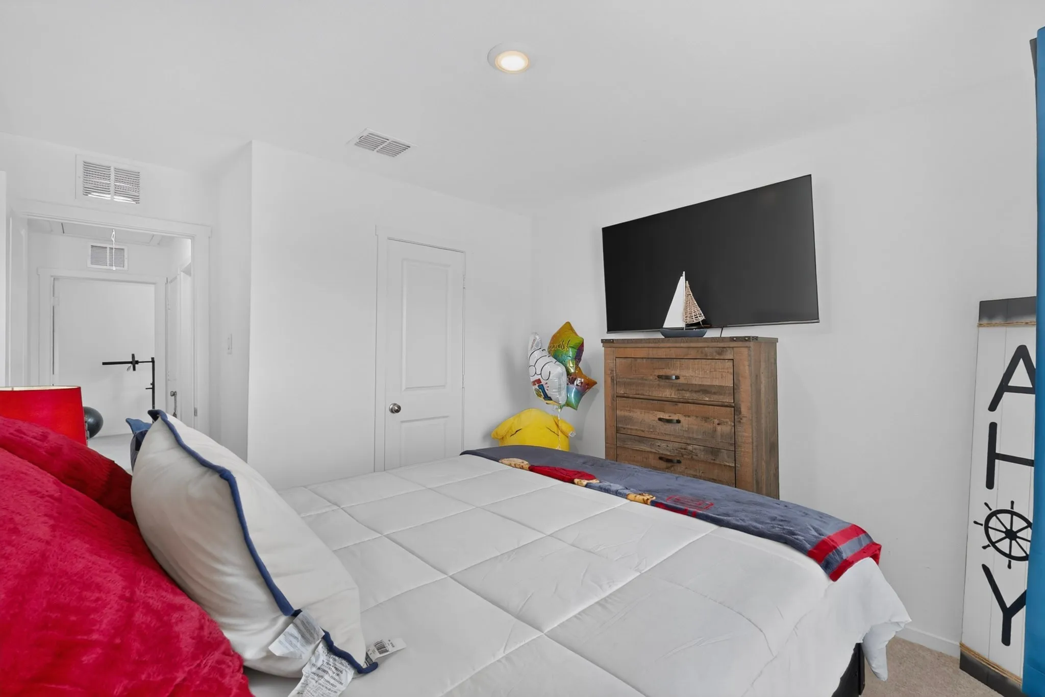 Recessed ceiling lighting, white interior walls, white paneled door, and wood-finish dresser