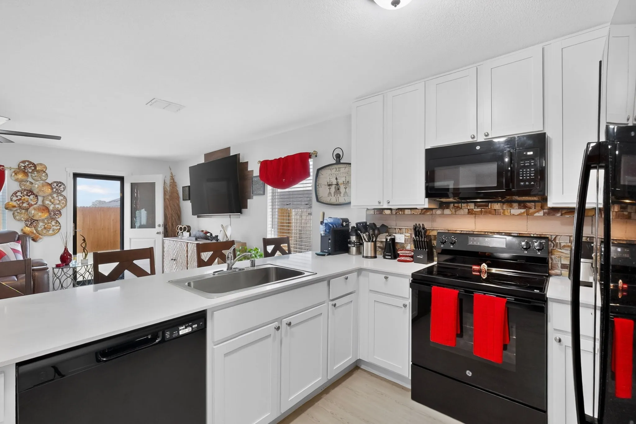 Open-concept kitchen featuring white cabinetry, light countertops, black appliances, a double basin sink, and wood-finish flooring