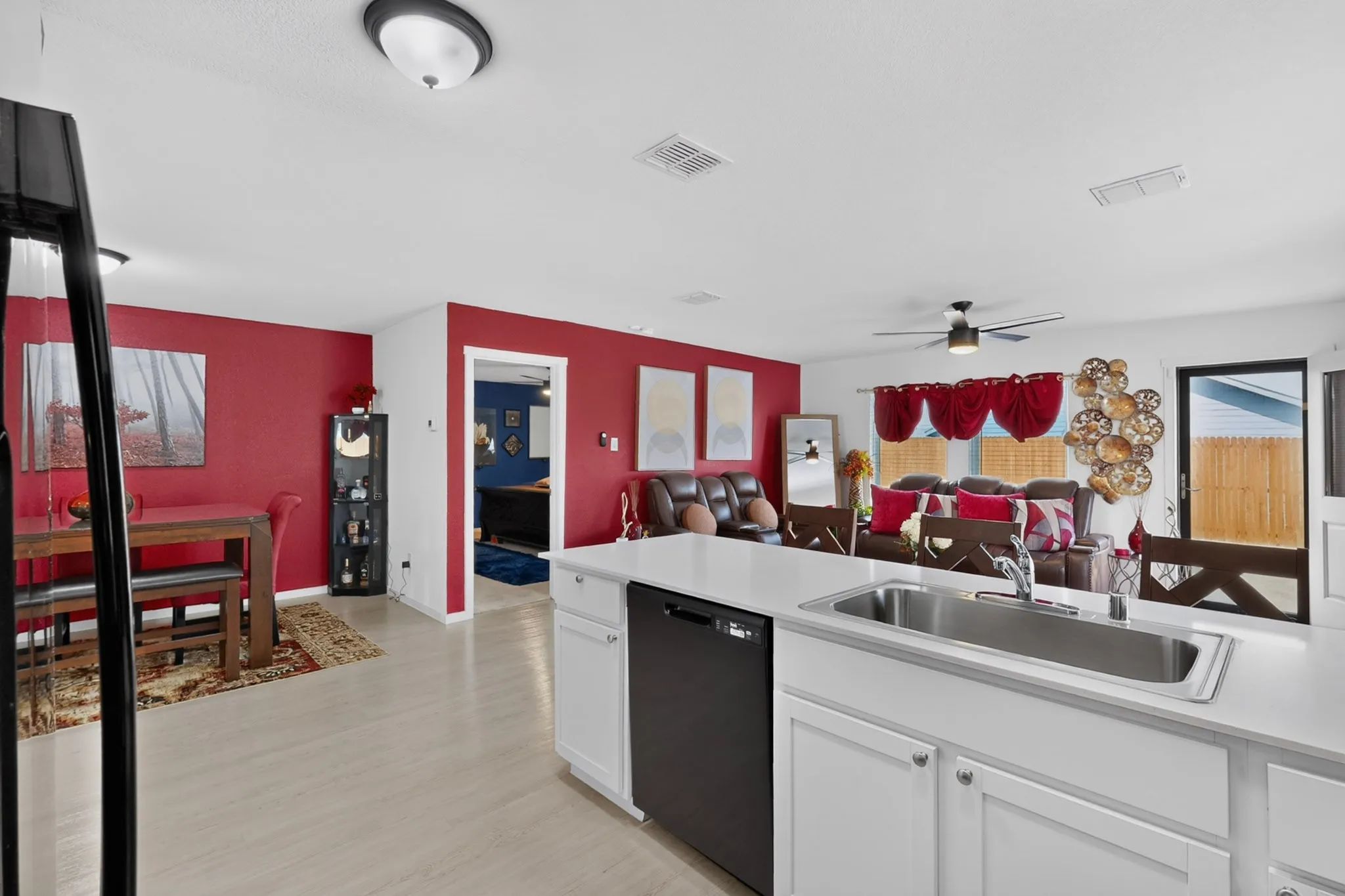 Kitchen island with integrated stainless steel sink, white cabinetry, and a black built-in dishwasher