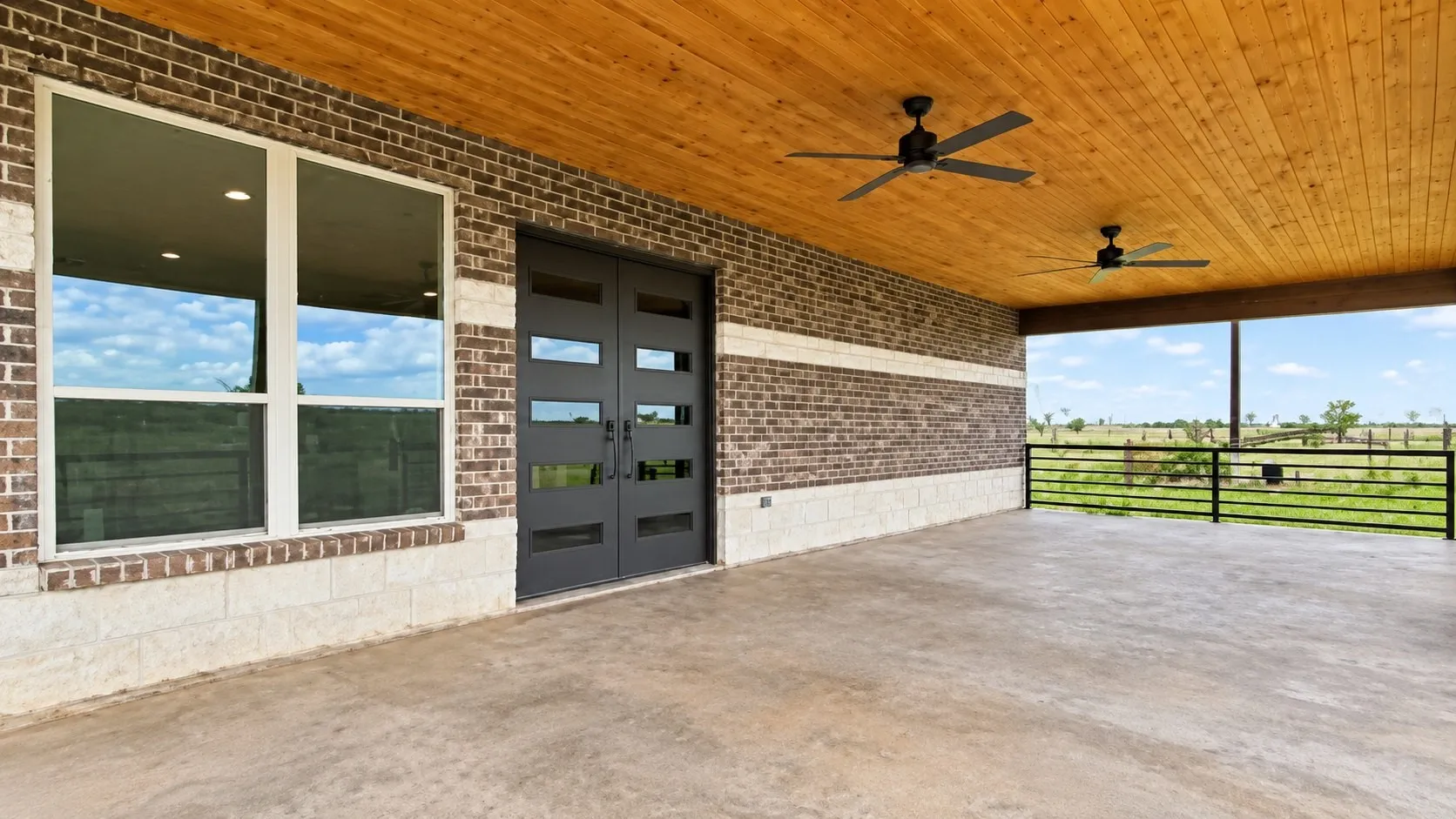 Expansive covered patio with a wood-finish ceiling, dual ceiling fans, and concrete flooring