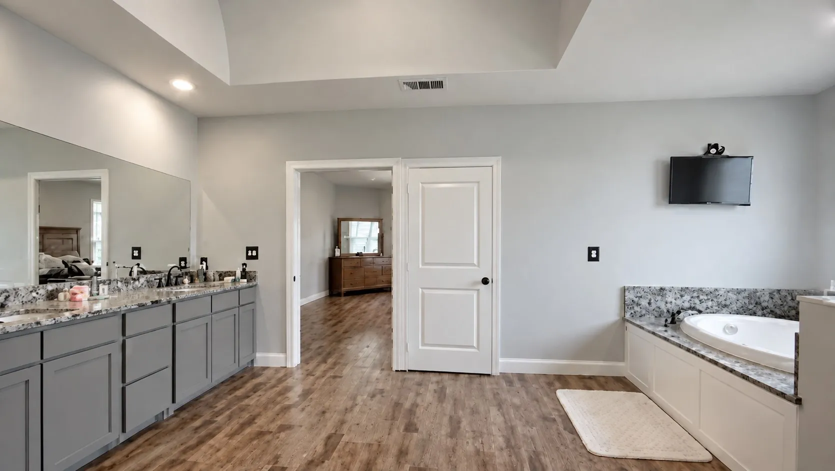 Expansive bathroom featuring wood-finish flooring, a double vanity with granite countertops, a built-in soaking tub with granite surround, and recessed lighting