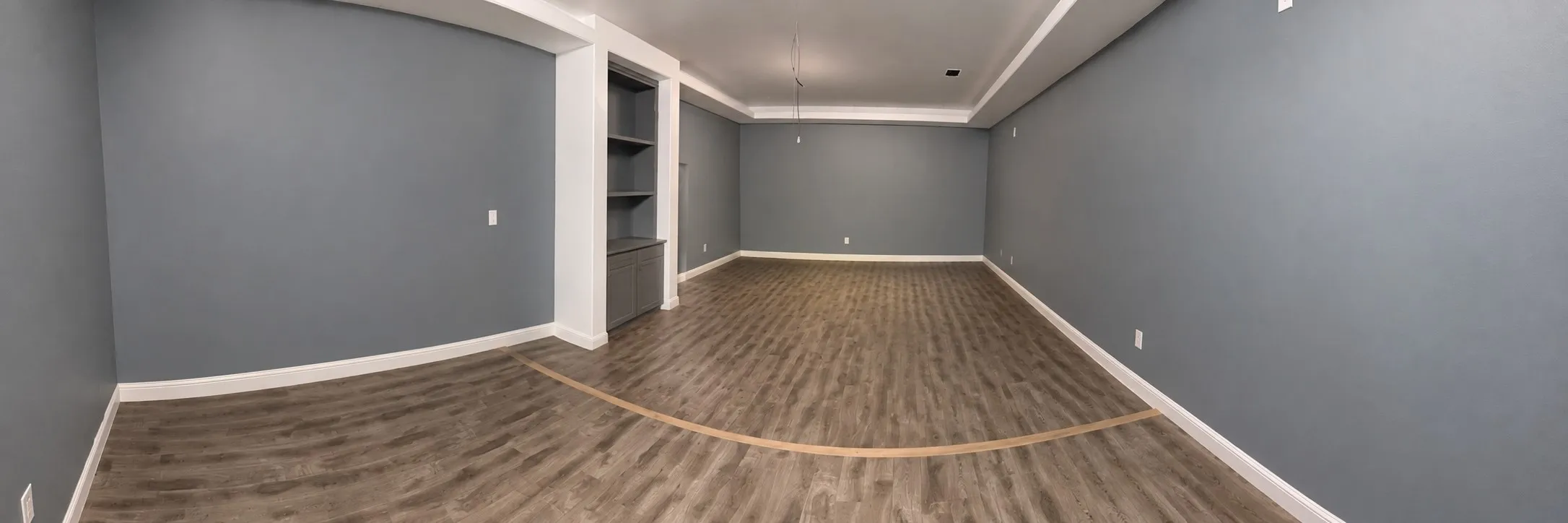 Spacious room featuring wood-finish flooring, built-in shelving, and crown molding