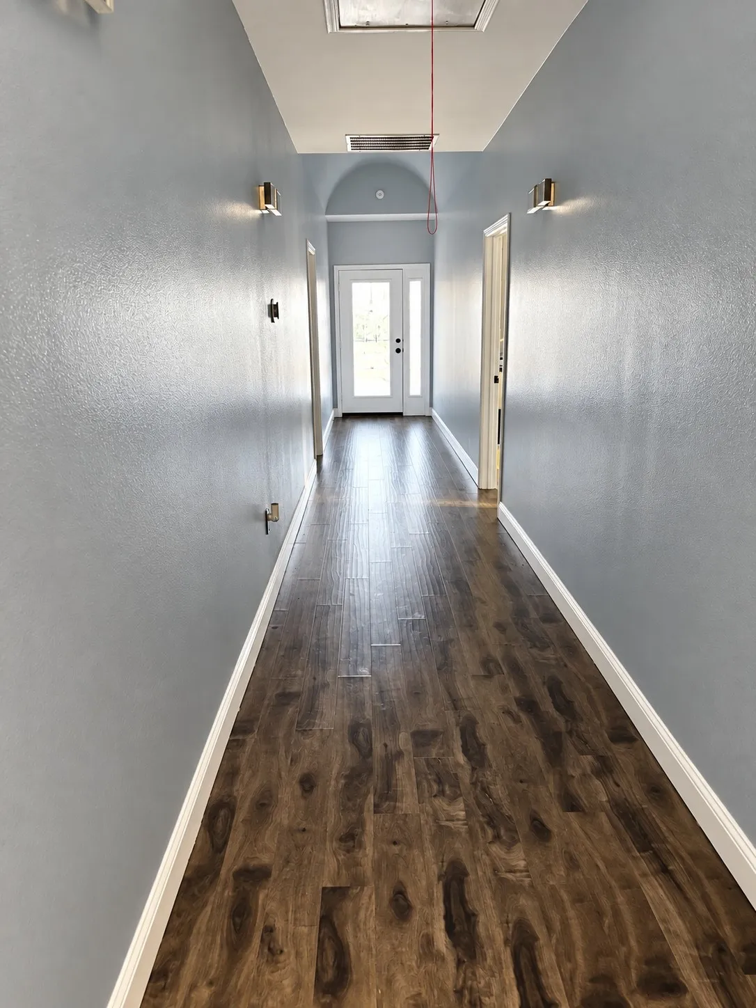 Hallway with wood-finish flooring, light grey walls, and wall-mounted sconces