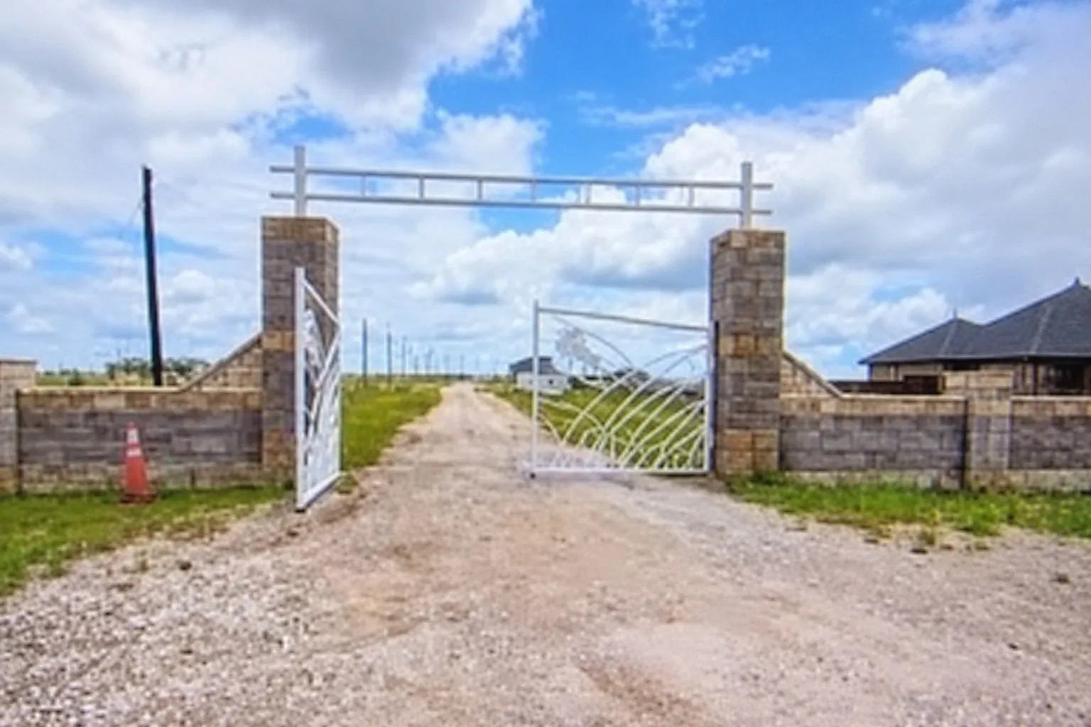Gated property entrance with stone pillars, decorative metal gates, and a gravel driveway