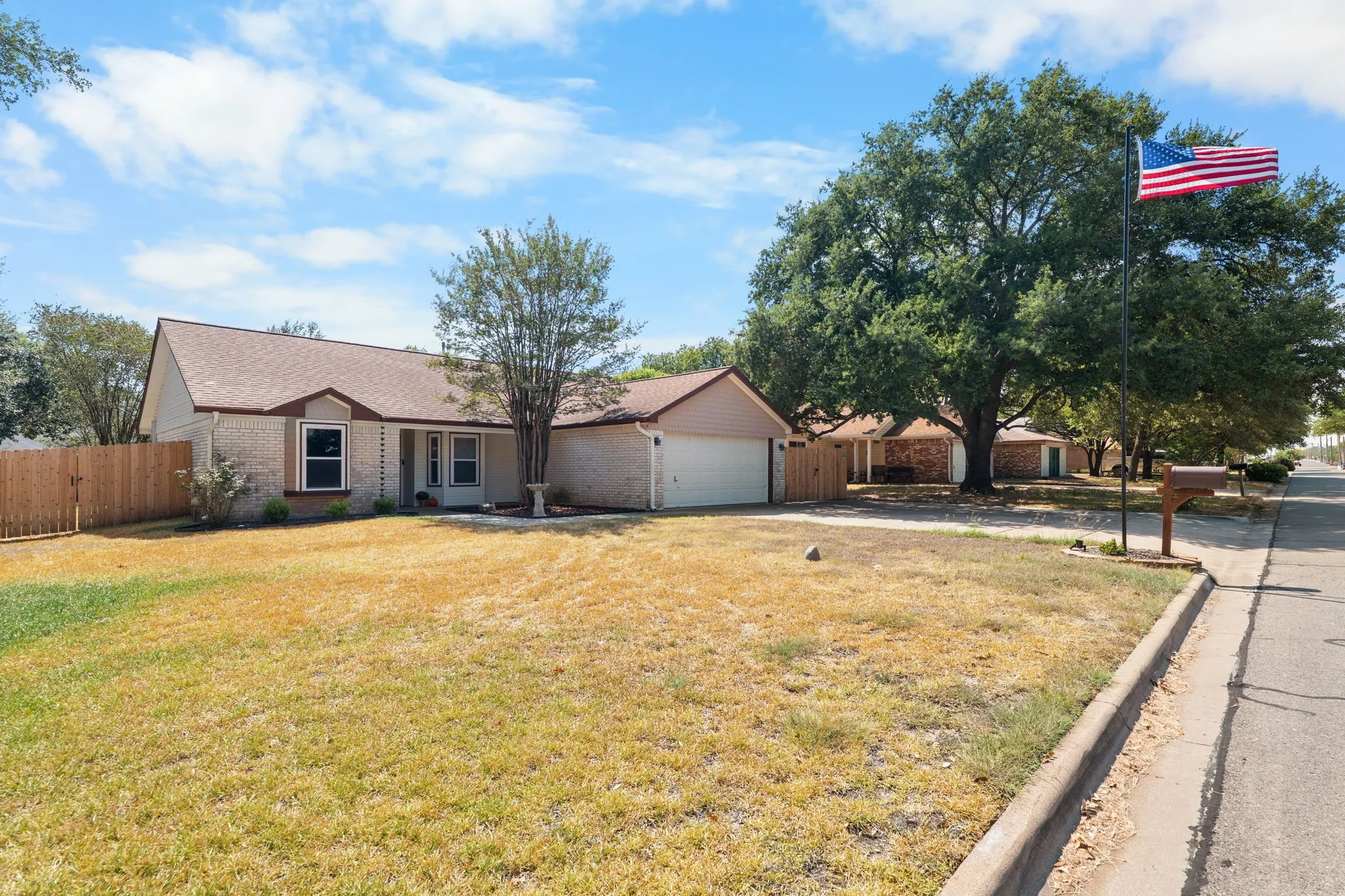 Brick exterior with an attached garage, a pitched roof, and a wooden privacy fence