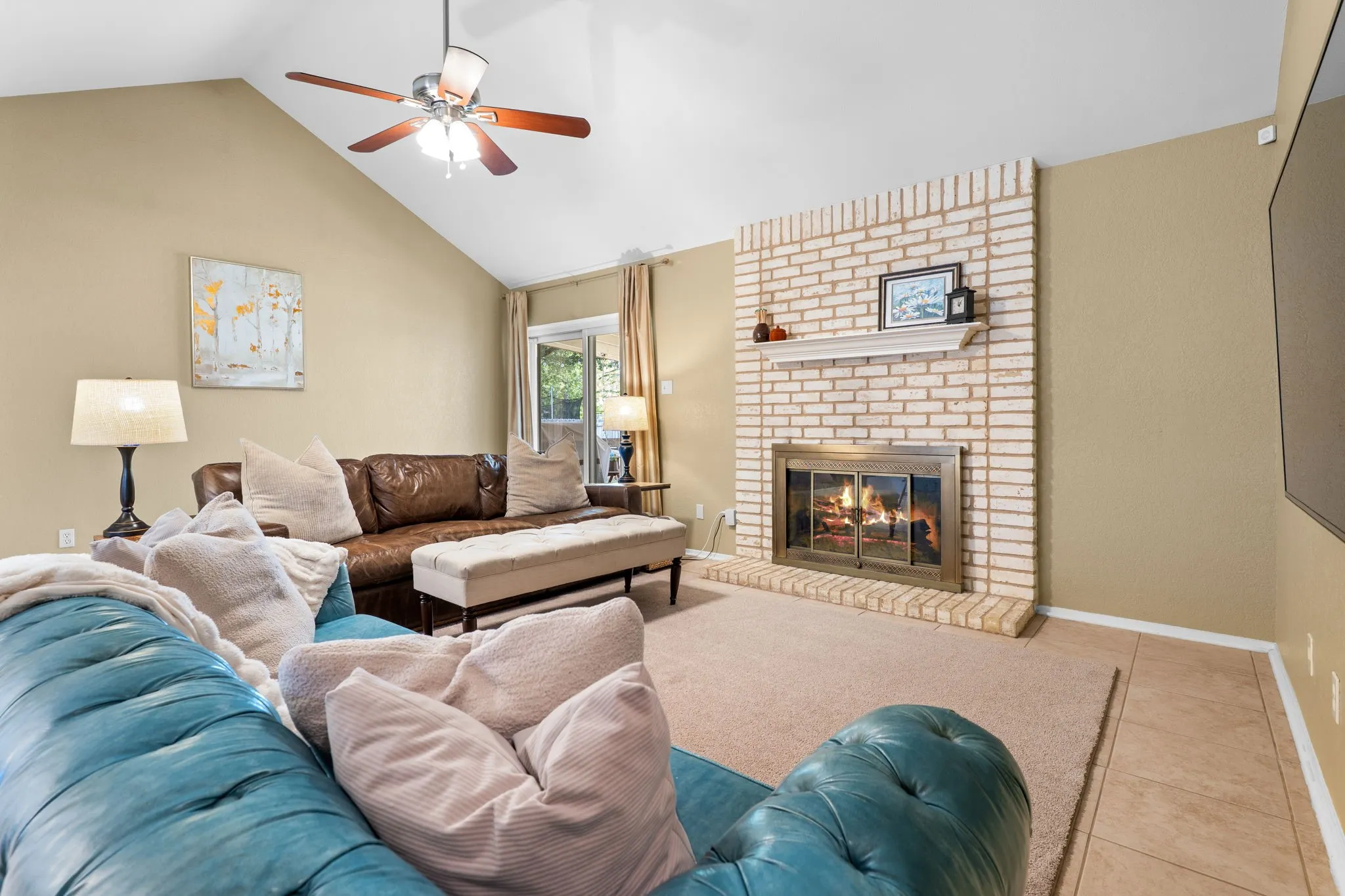 Vaulted ceiling with a ceiling fan, brick fireplace with a mantel, and sliding glass door