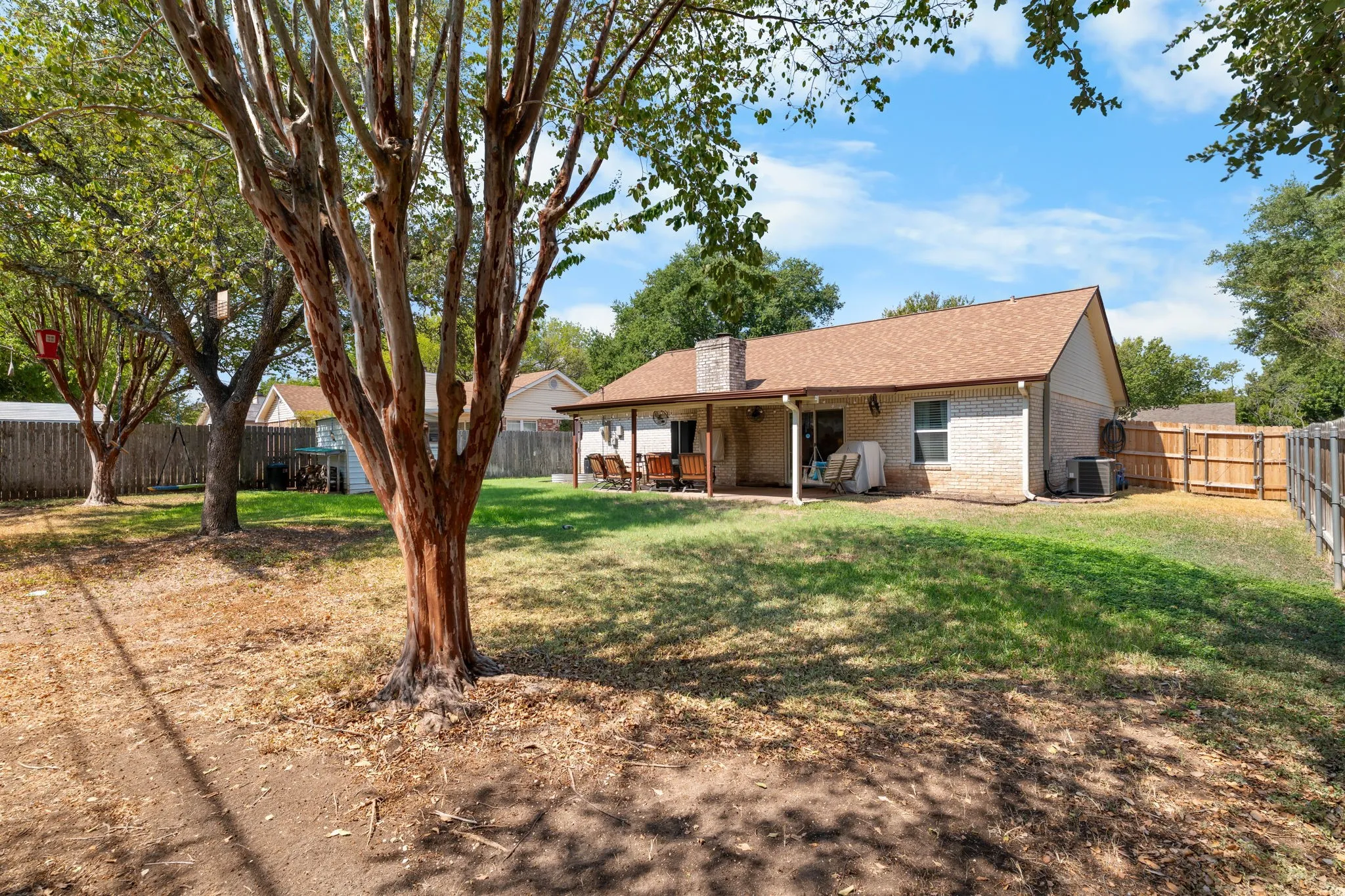 Expansive backyard featuring mature trees, a covered patio, and a privacy fence