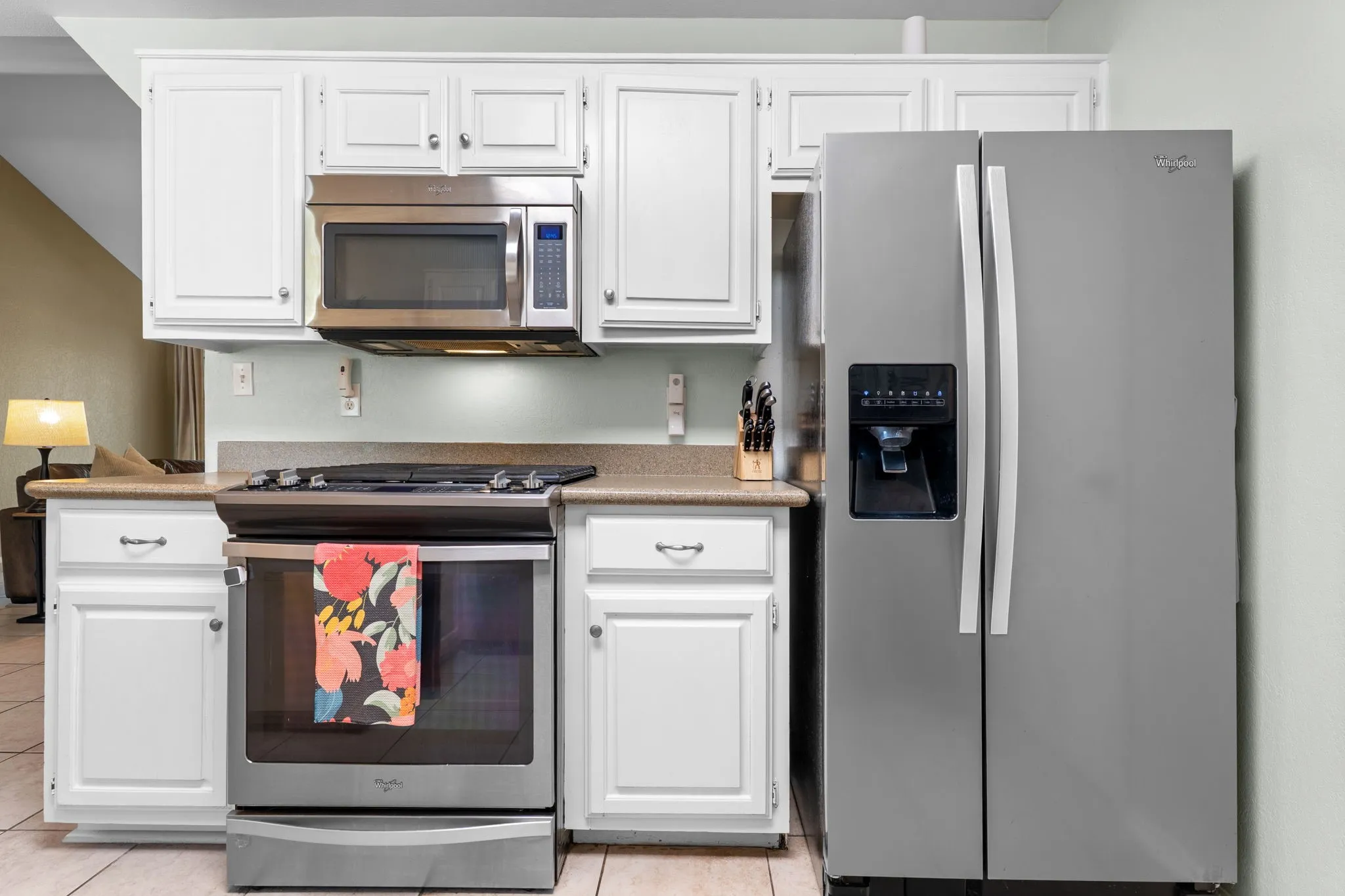 White cabinetry, stainless steel appliances, stone-finish countertops, and tile flooring