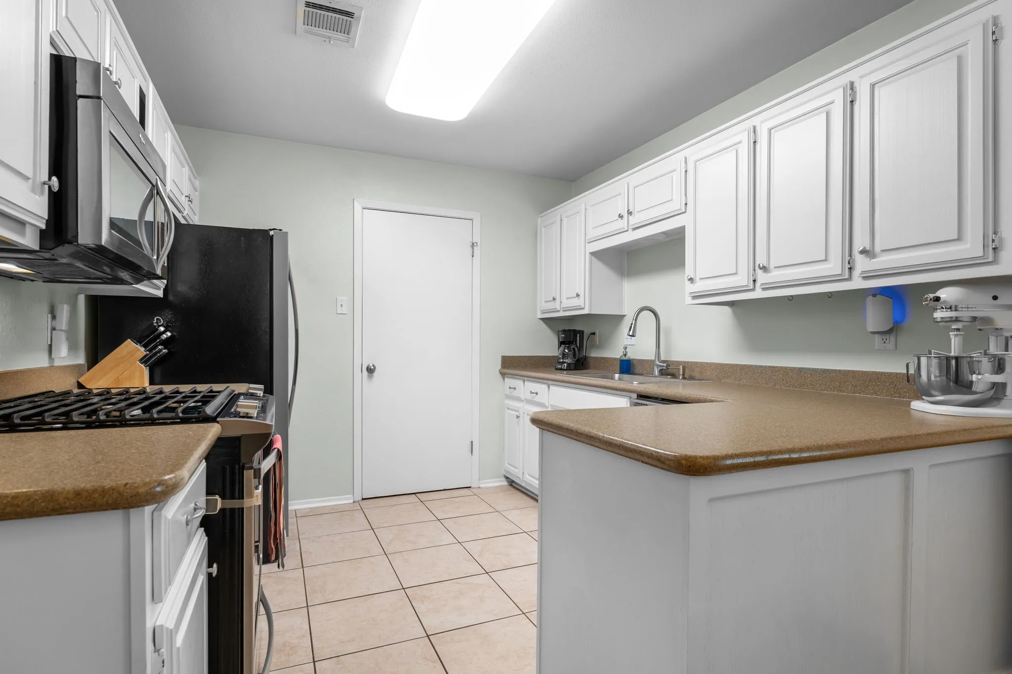 White cabinetry with brushed nickel hardware, light-toned countertops, and tile flooring