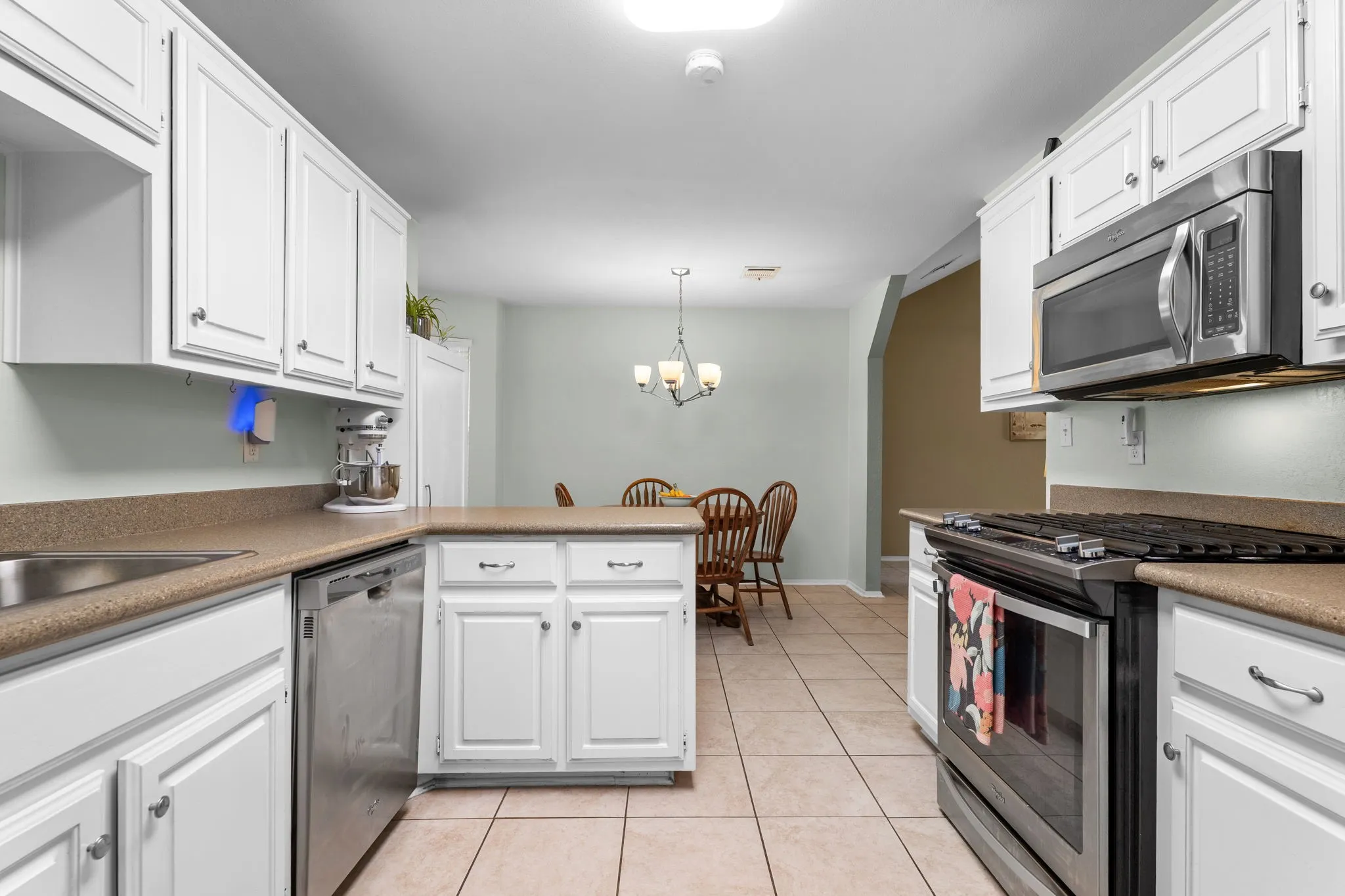 White cabinetry, stainless steel appliances, ceramic tile flooring, and solid surface countertops