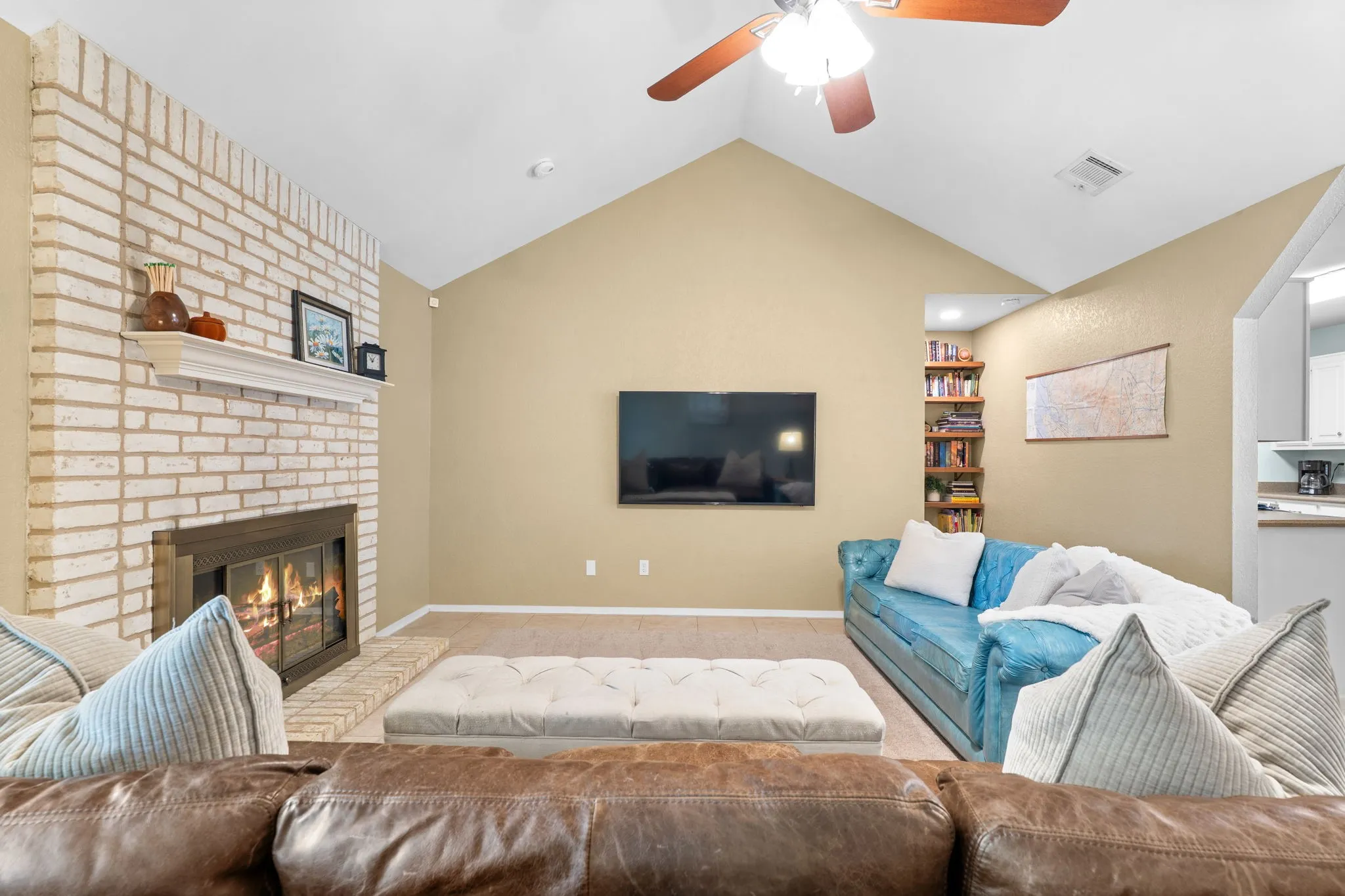 Vaulted ceiling with a ceiling fan, white brick fireplace with a mantel, built-in shelving, and carpeting
