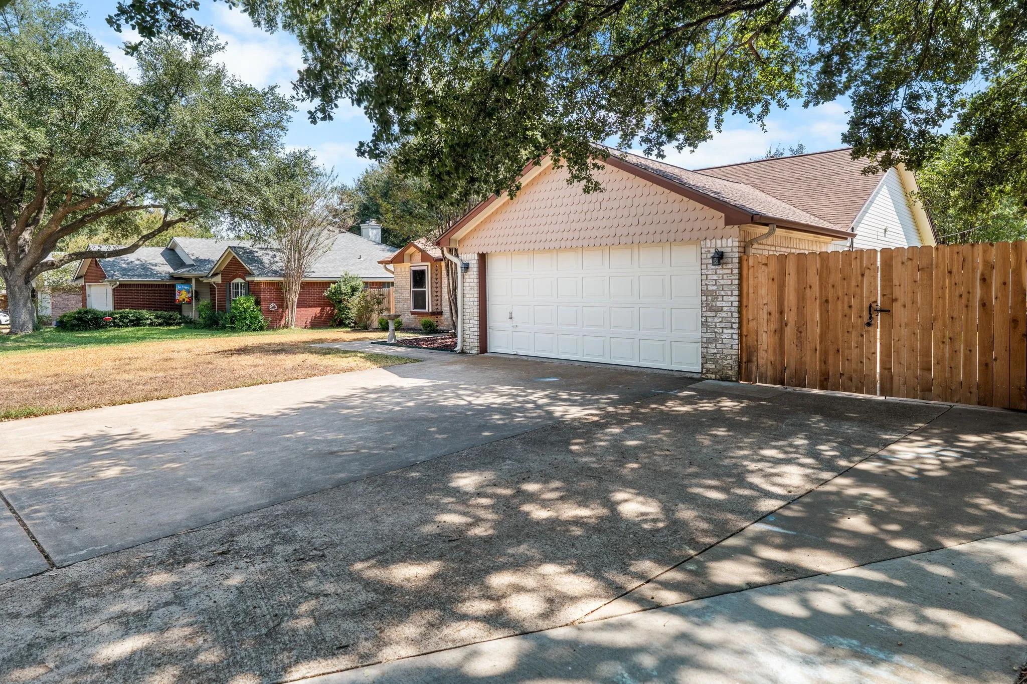 Expansive concrete driveway leading to an attached garage with a panel door, complemented by a wooden fence with a gate, and a brick veneer exterior