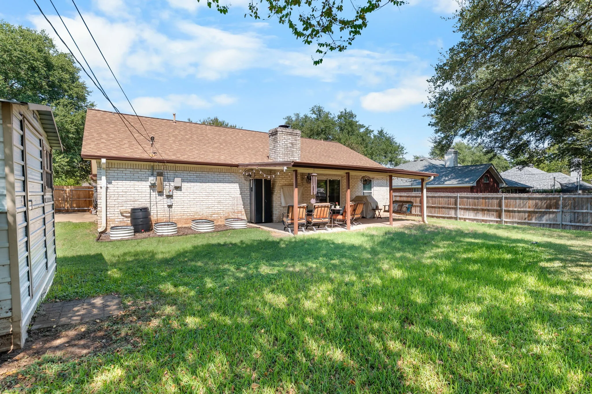 Expansive lawn with a covered patio, brick exterior, and a wood privacy fence