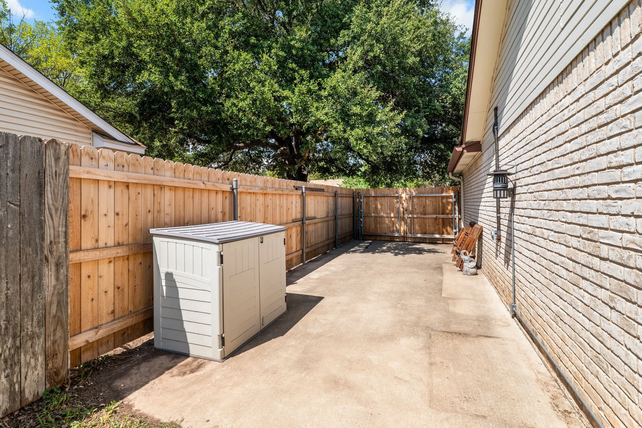 Outdoor concrete patio space featuring a wood fence, brick exterior siding, and an exterior light fixture