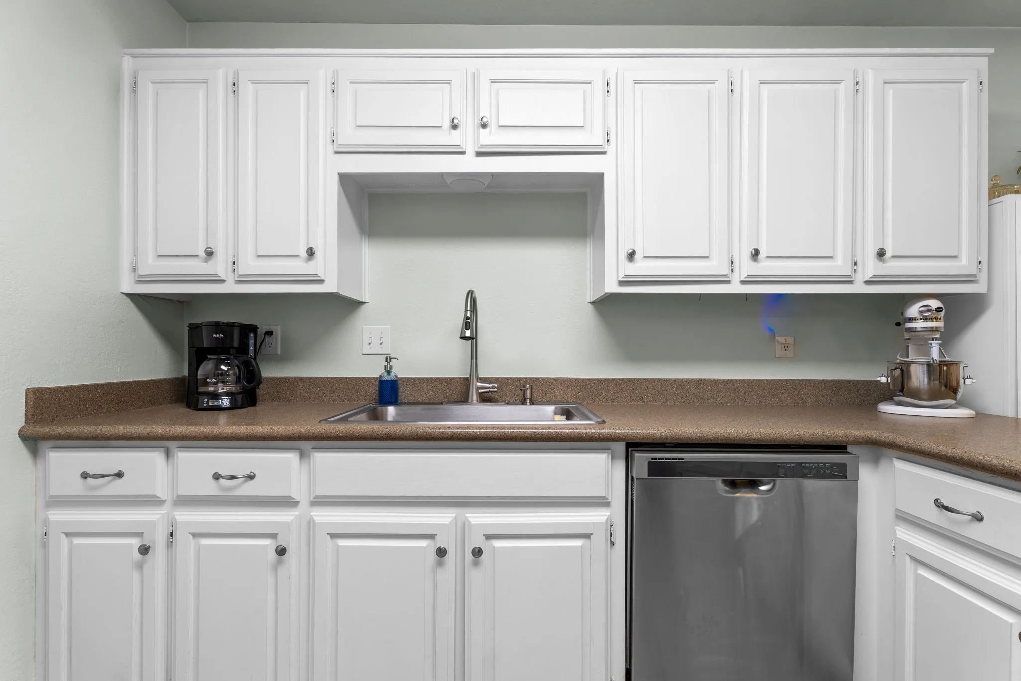 Bright kitchen featuring white cabinetry with recessed panel doors, warm wood-finish countertops, stainless steel appliances including a dishwasher, and a single-basin sink with chrome faucet
