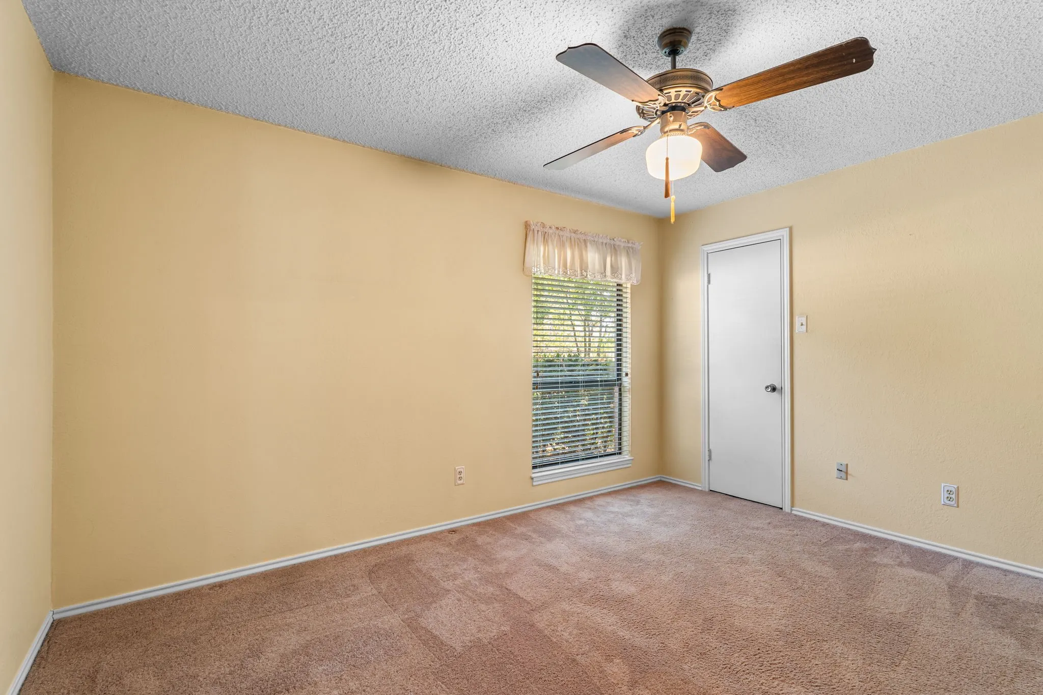 Textured ceiling, ceiling fan with integrated lighting, carpeted flooring, window with blinds, and a white interior door