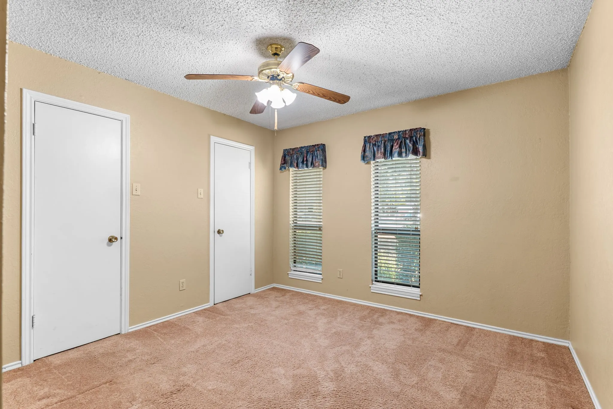 Carpeted flooring, ceiling fan with integrated lighting, two windows with blinds, and multiple doors
