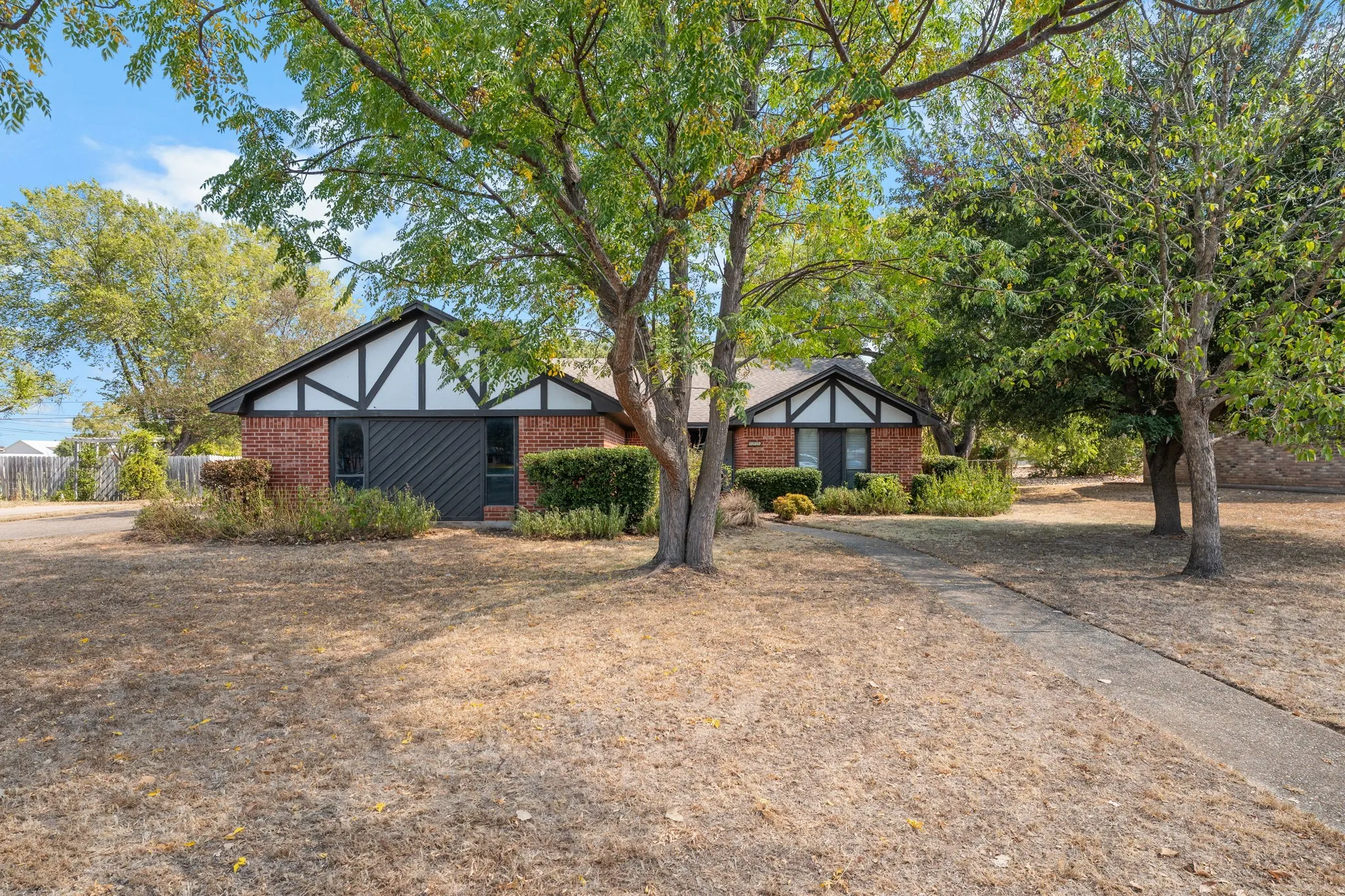 Brick exterior with white and dark trim, gabled roofline, and established trees