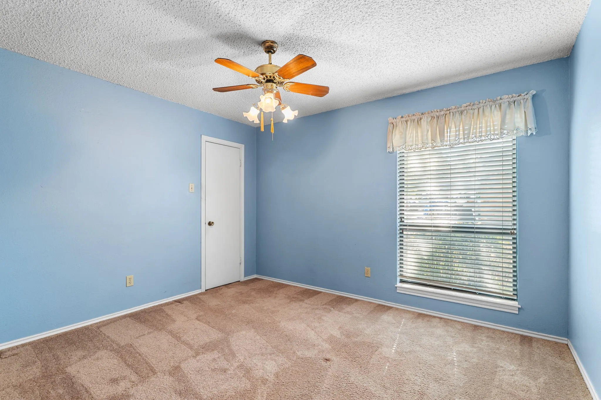 Ceiling fan with integrated lighting, window with blinds, light blue painted walls, wall-to-wall carpeting, and white trim