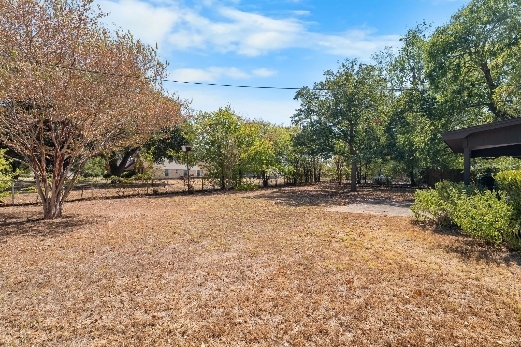 Expansive property featuring mature trees, a partially paved area, and a sloped roofline structure
