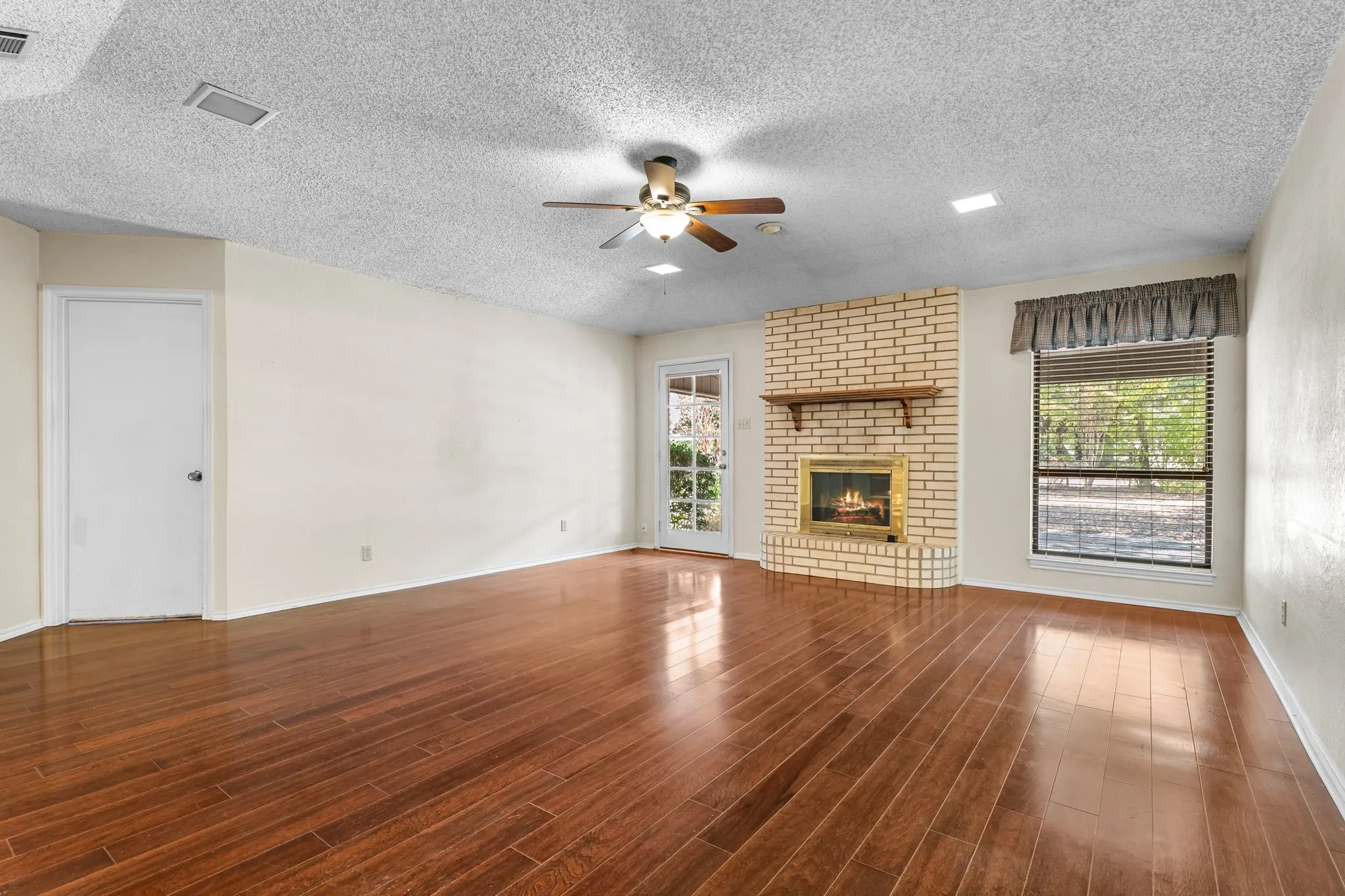 Spacious room featuring wood-finish flooring, a brick fireplace with a mantel, a ceiling fan with integrated lighting, and recessed ceiling lights