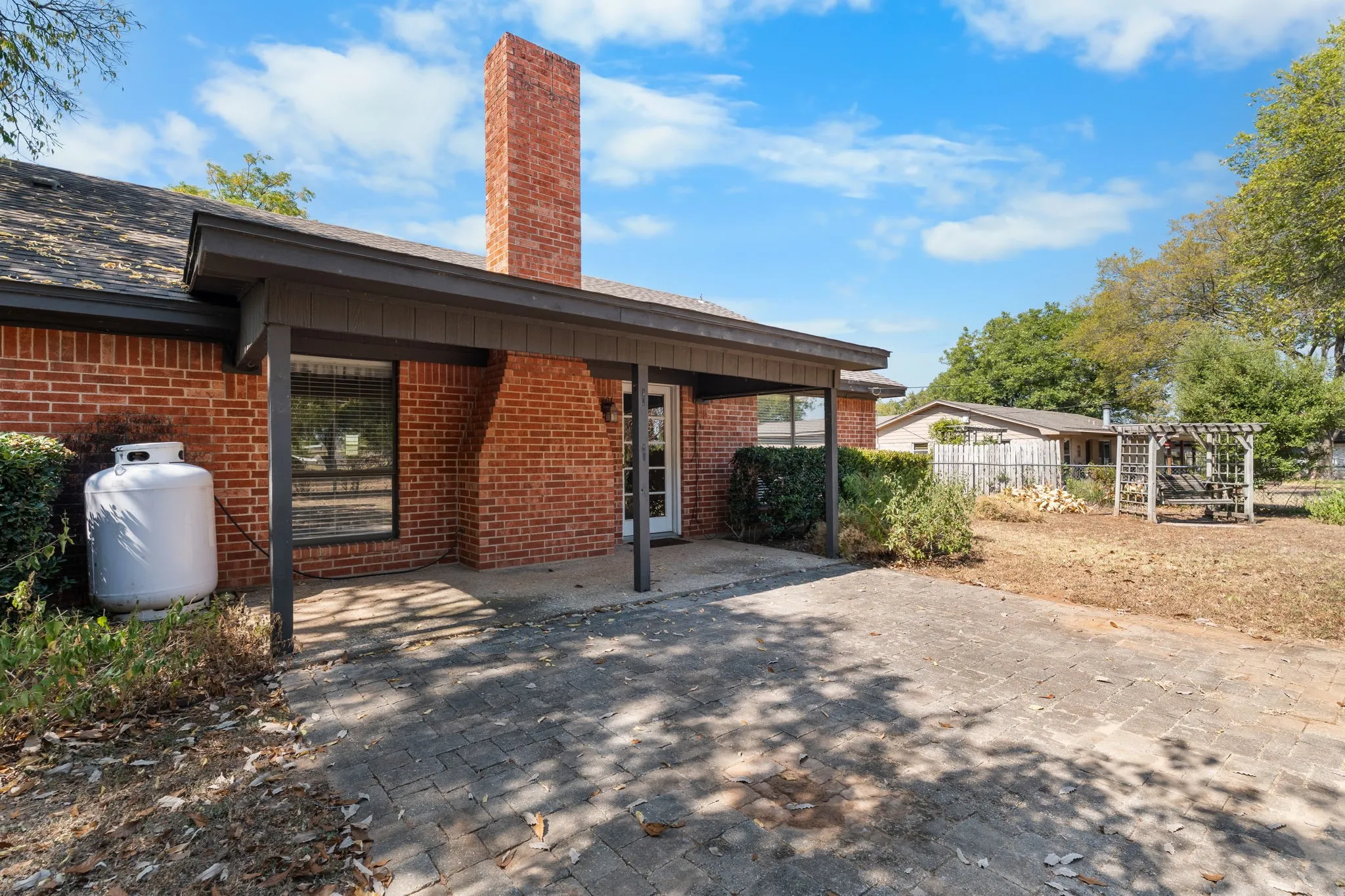 Brick exterior with a covered patio, exposed brick chimney, and paved patio area