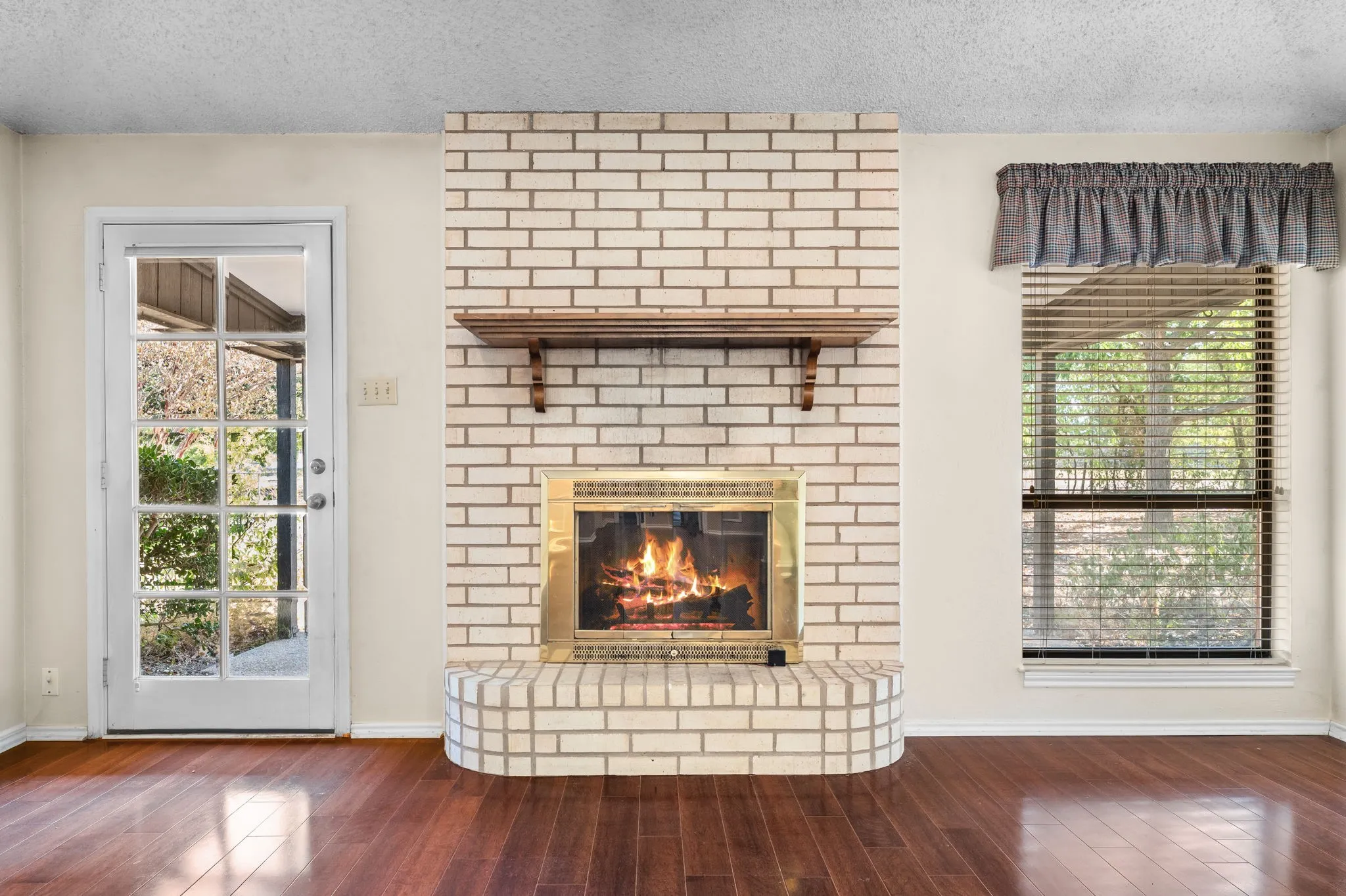 Brick fireplace with a brass-trimmed firebox and wood mantel shelf, complemented by rich wood-finish flooring