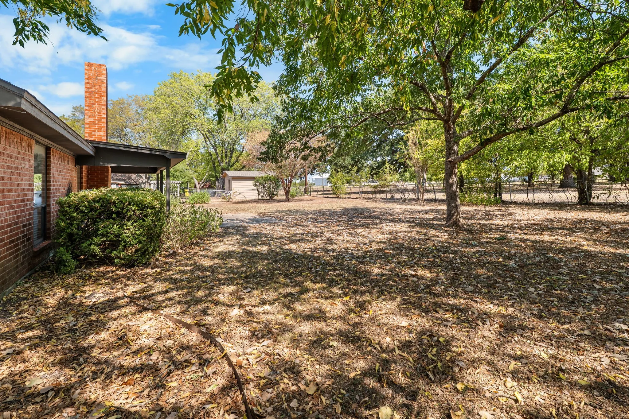 Expansive yard with mature trees, brick exterior, and covered patio
