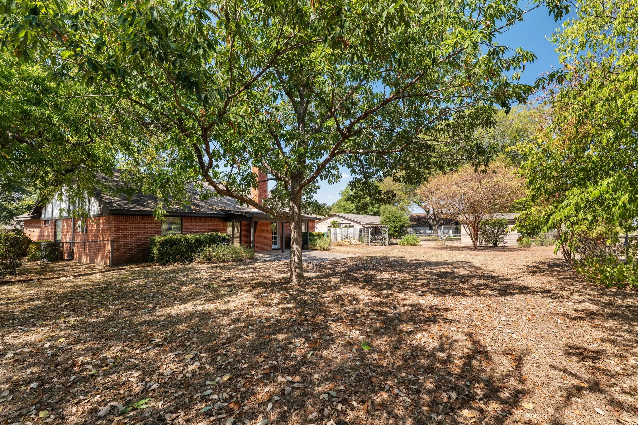 Expansive outdoor space featuring a mature tree, brick exterior, and established landscaping