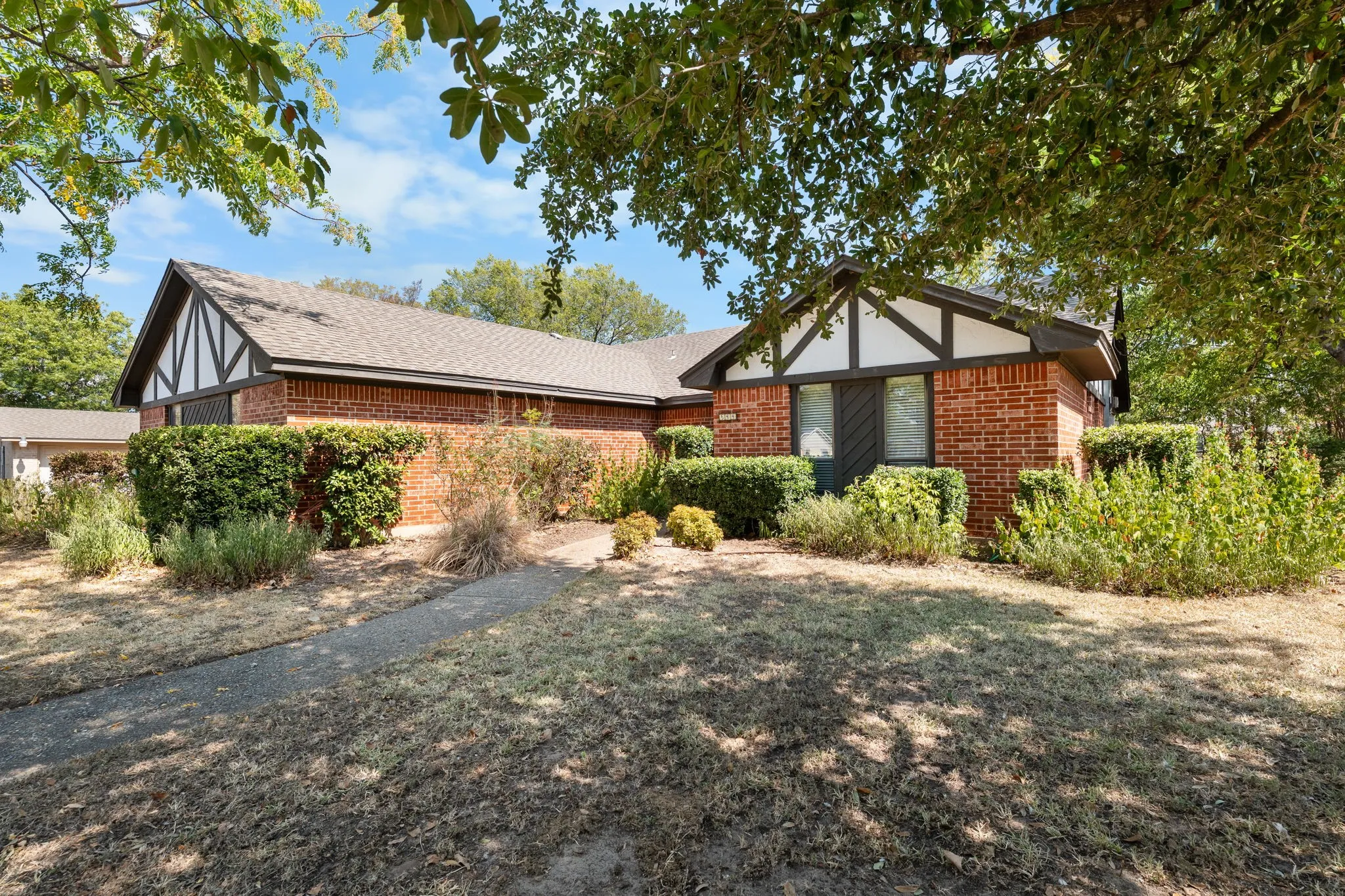 Brick exterior featuring white and dark trim, gabled roofline, and established shrubbery