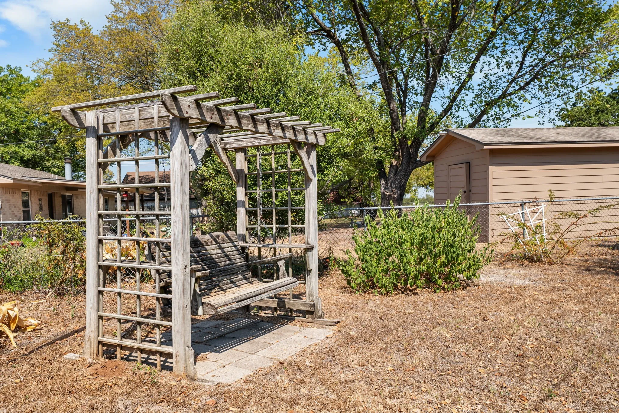Wood pergola with integrated swing bench, paver base, and rear storage shed
