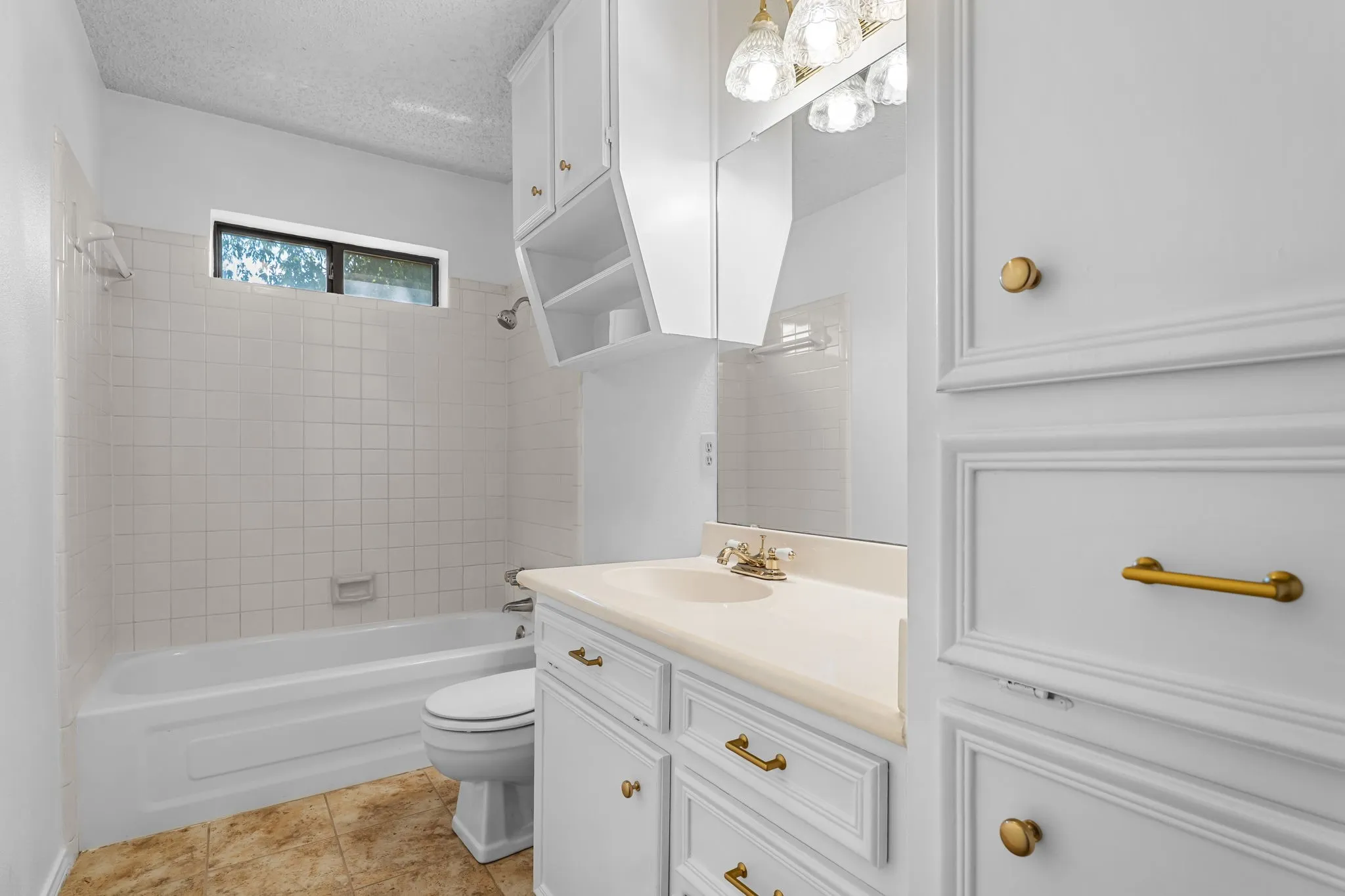 White paneled cabinetry with brass hardware, light-colored countertop, integrated sink, and overhead vanity lighting