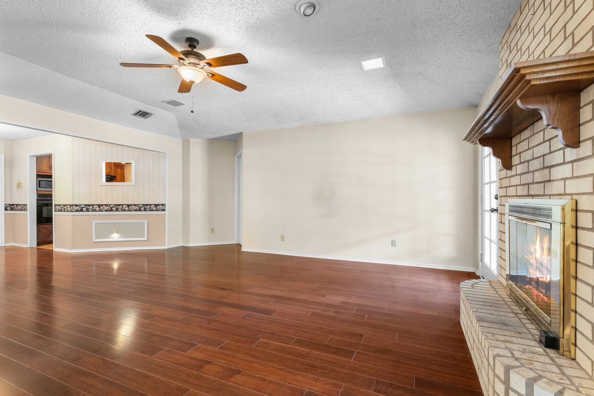 Wood-finish flooring, brick fireplace with a wood mantle, vaulted ceiling, and a ceiling fan with integrated lighting