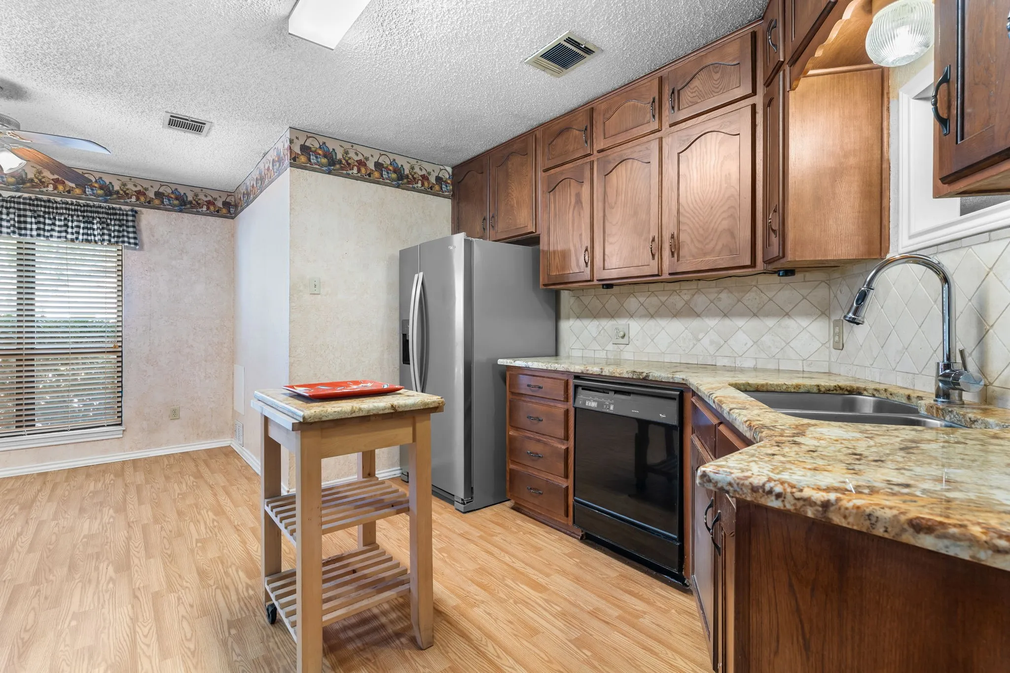 Kitchen featuring wood-finish flooring, wood cabinetry, stone countertops, stainless steel sink, and a ceiling fan
