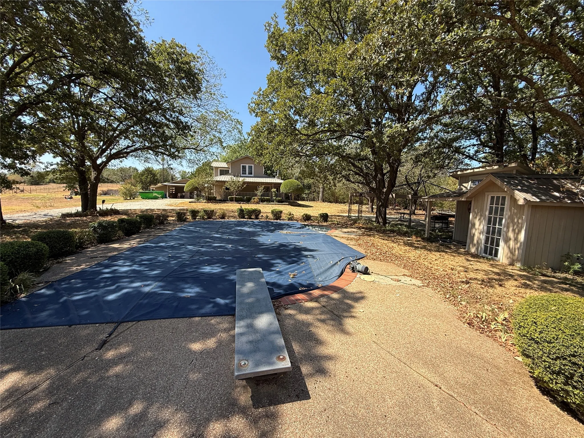 Outdoor swimming pool with a diving board, surrounded by mature trees and shrubs