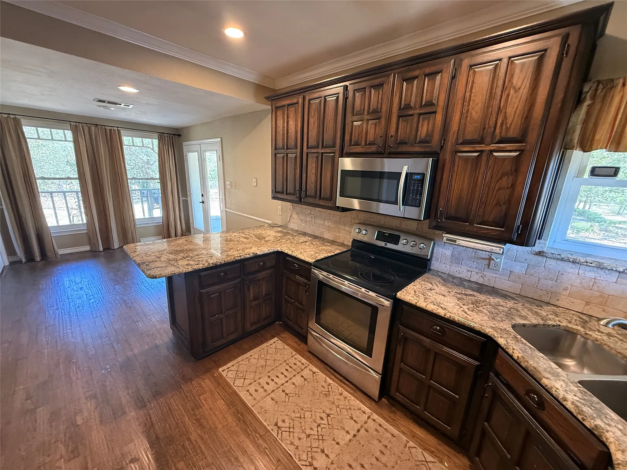 Kitchen featuring wood-finish flooring, dark wood cabinetry, stainless steel appliances, speckled stone countertops, and a subway tile backsplash