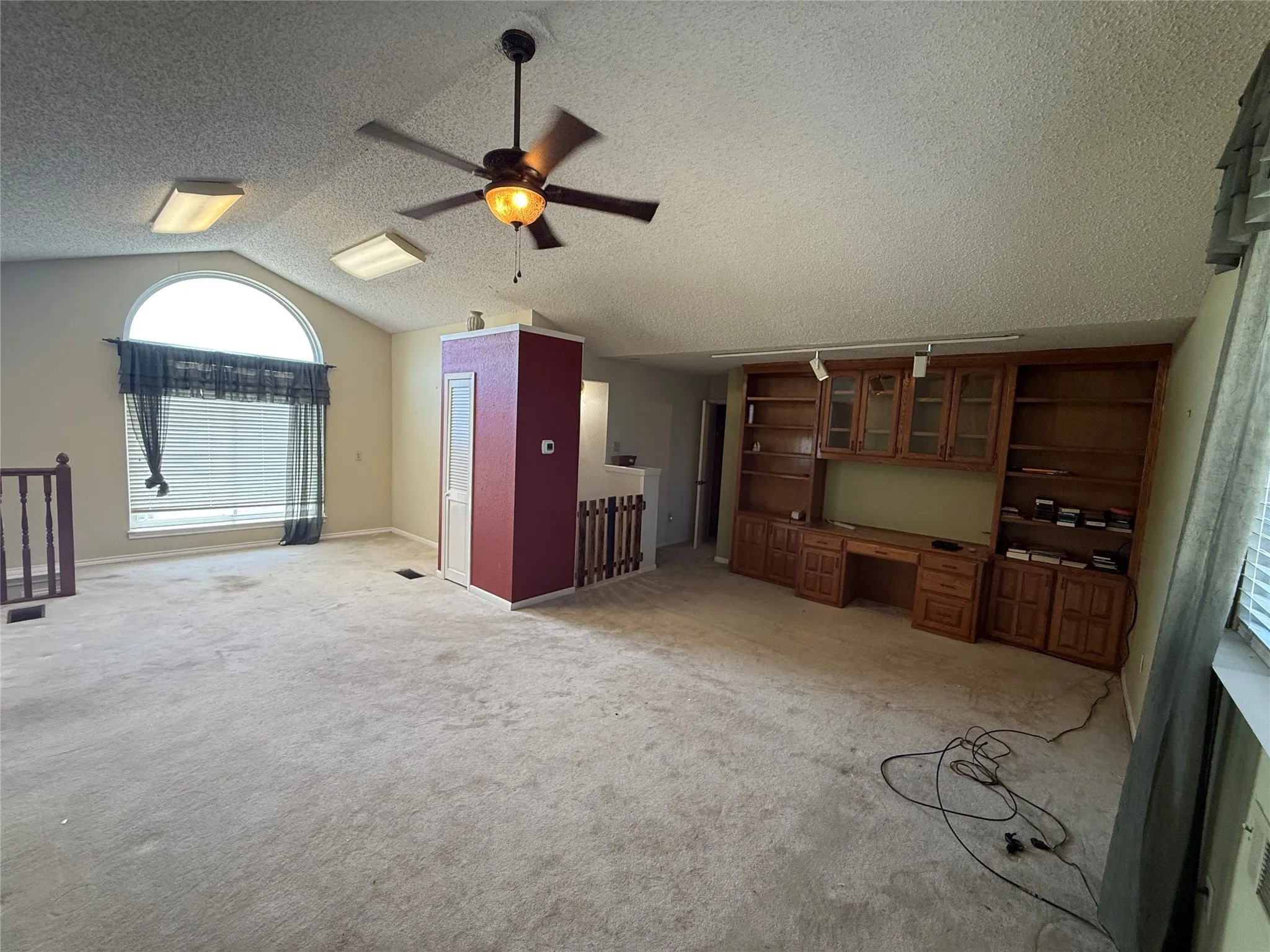 Vaulted ceiling with ceiling fan, arched window with blind, built-in wooden cabinetry with glass-front uppers, and track lighting