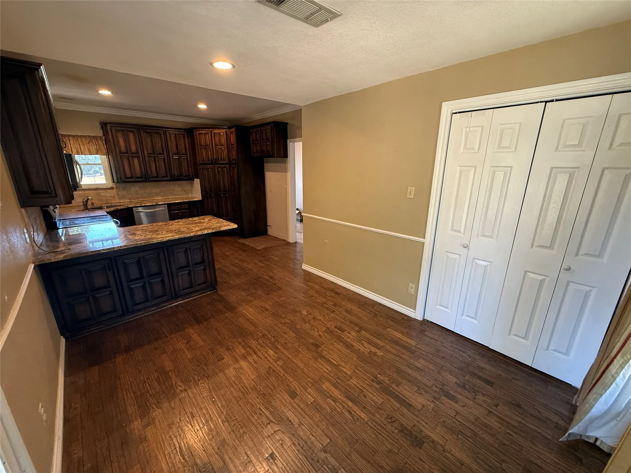 Kitchen featuring dark wood-finish cabinetry, light-toned granite countertops, and a stone-finish backsplash