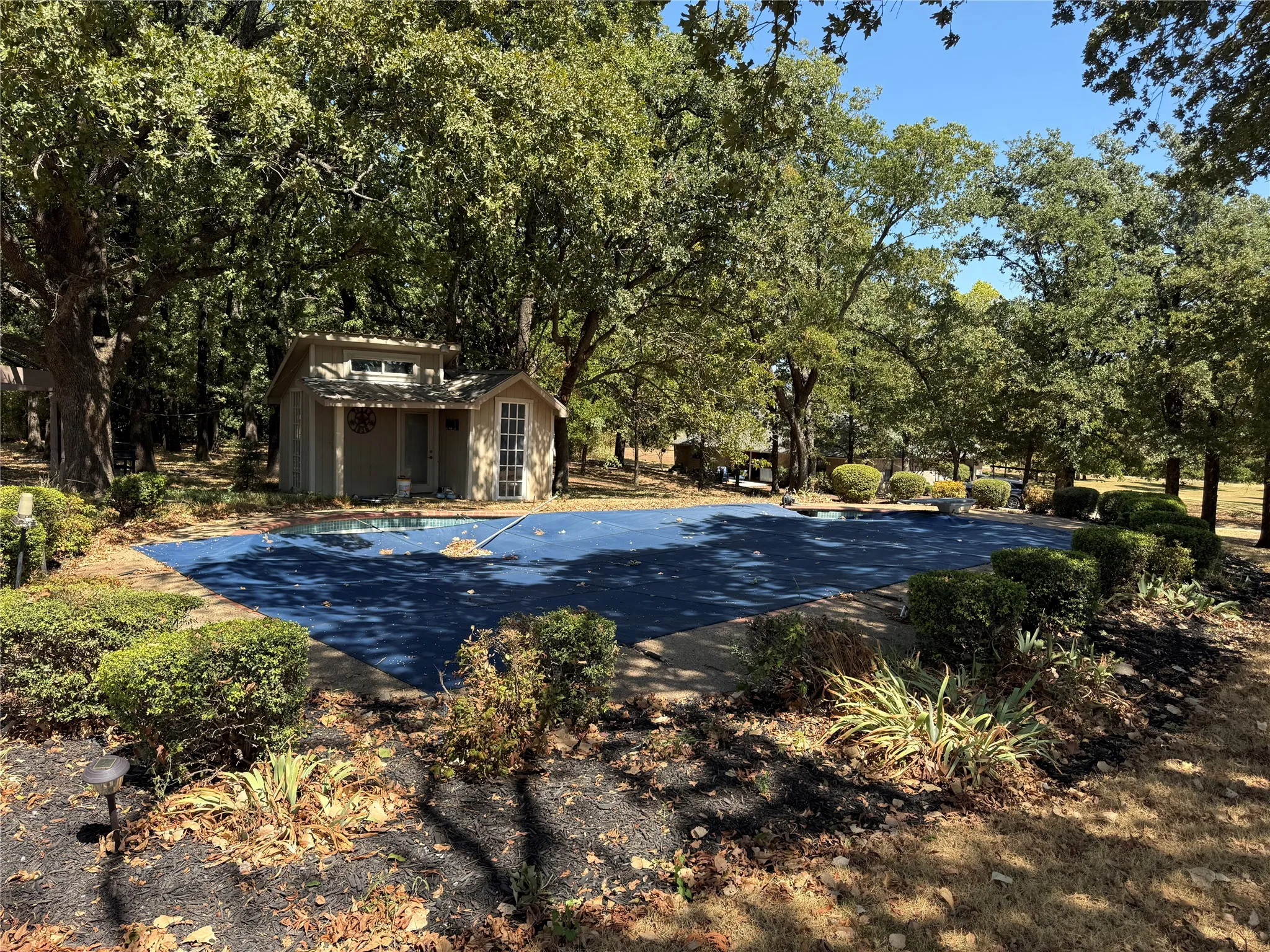 Covered swimming pool with surrounding landscaping and mature trees