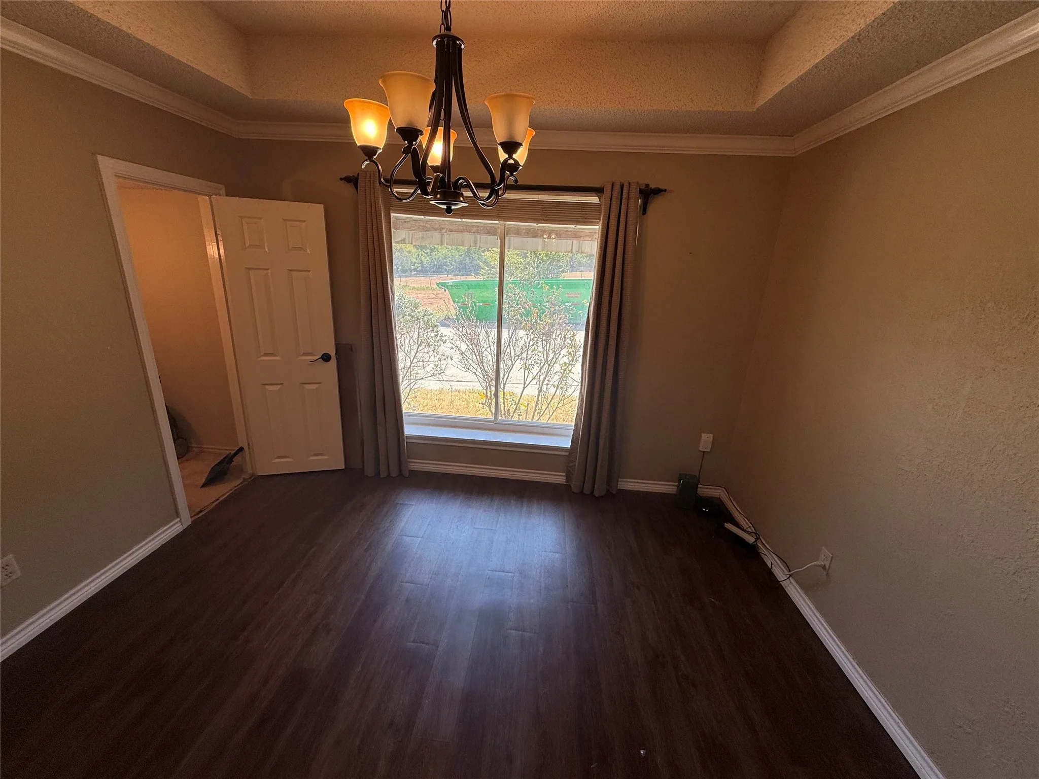 Tray ceiling with crown molding, wood-finish flooring, chandelier lighting, and a large window