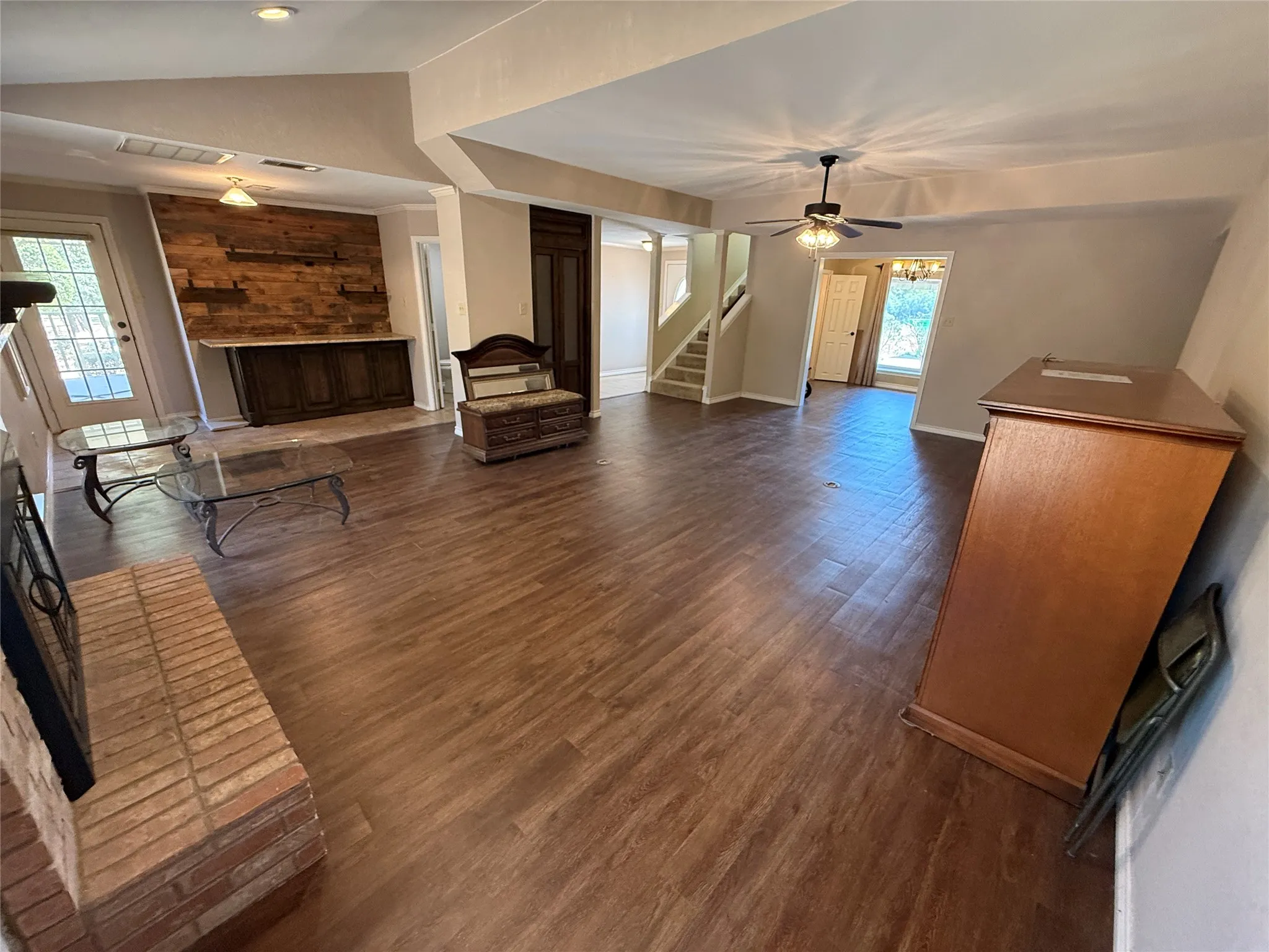 Wood-finish flooring throughout, brick fireplace, built-in wooden cabinetry with a light-toned countertop, and a wood-paneled accent wall