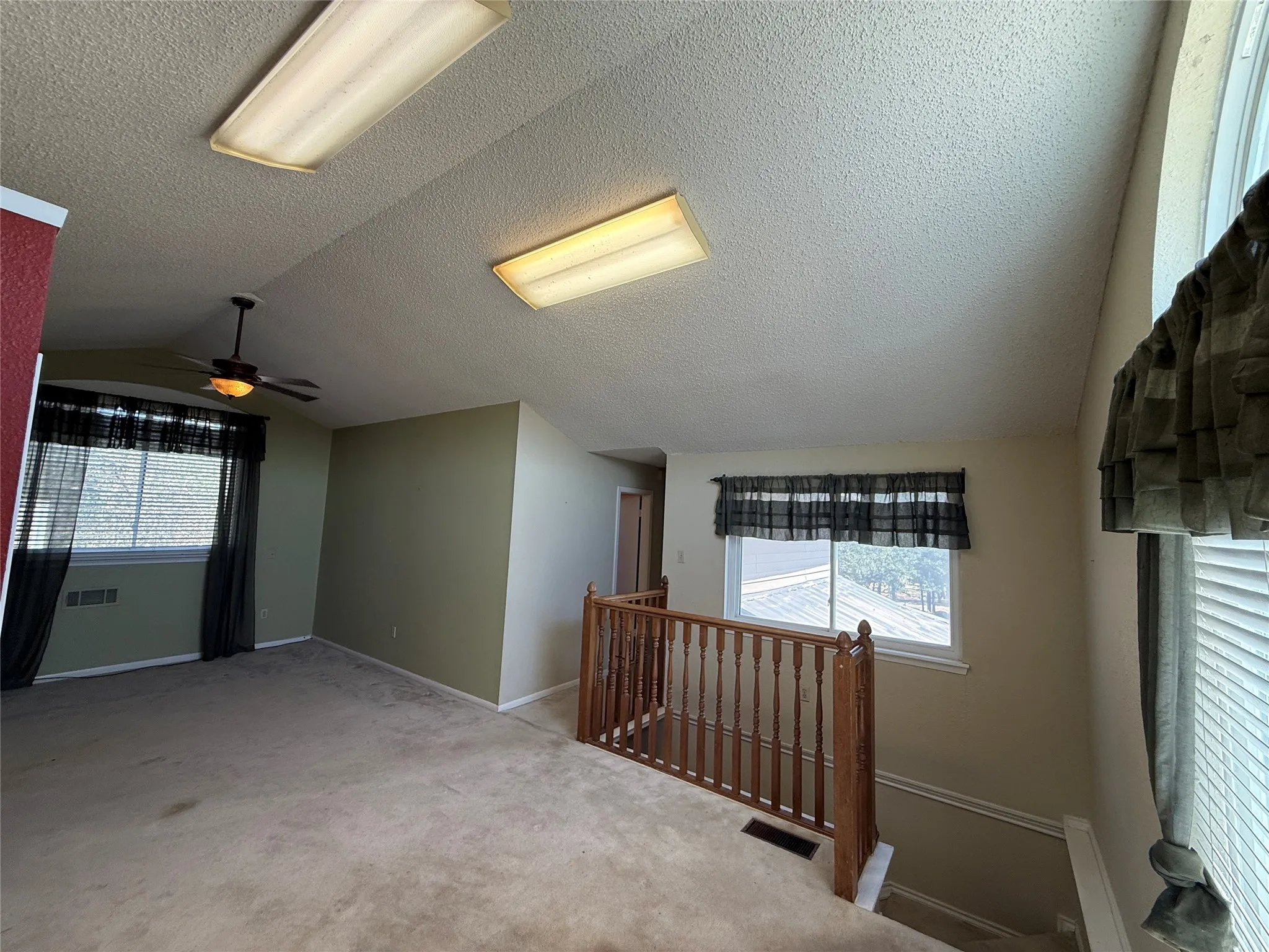 Vaulted ceiling with a ceiling fan, carpeted flooring, and a wood spindle railing