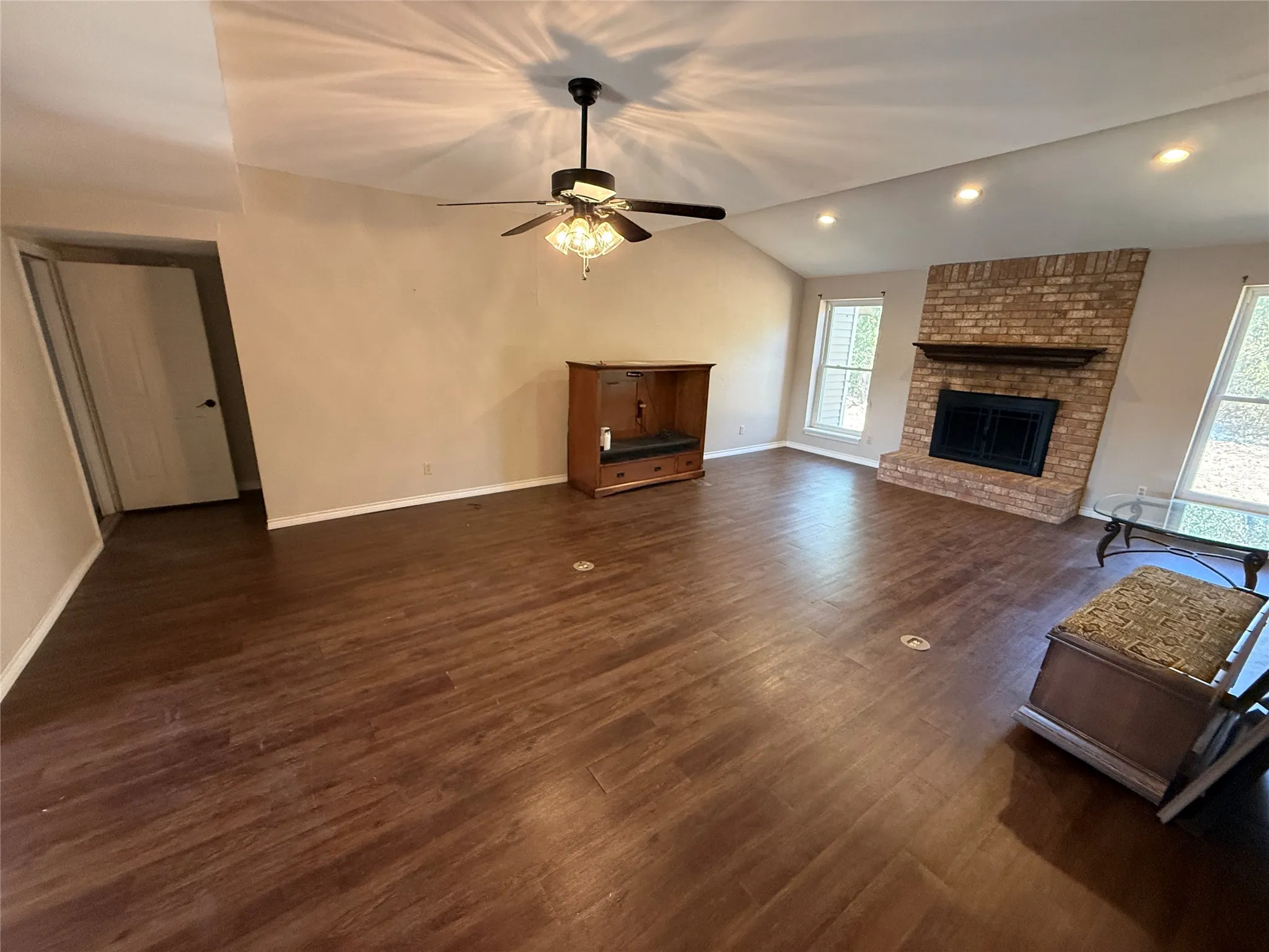 Vaulted ceiling with a ceiling fan, wood-finish flooring, brick-surround fireplace with a mantel, and recessed lighting
