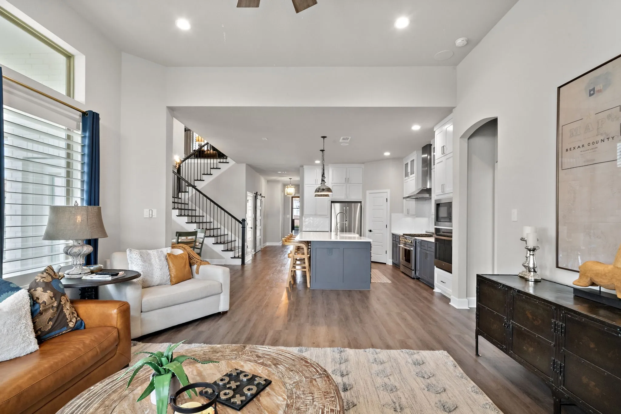 Open-concept living area with wood-finish flooring, a contemporary kitchen island, built-in stainless steel appliances, and a staircase with a black metal railing