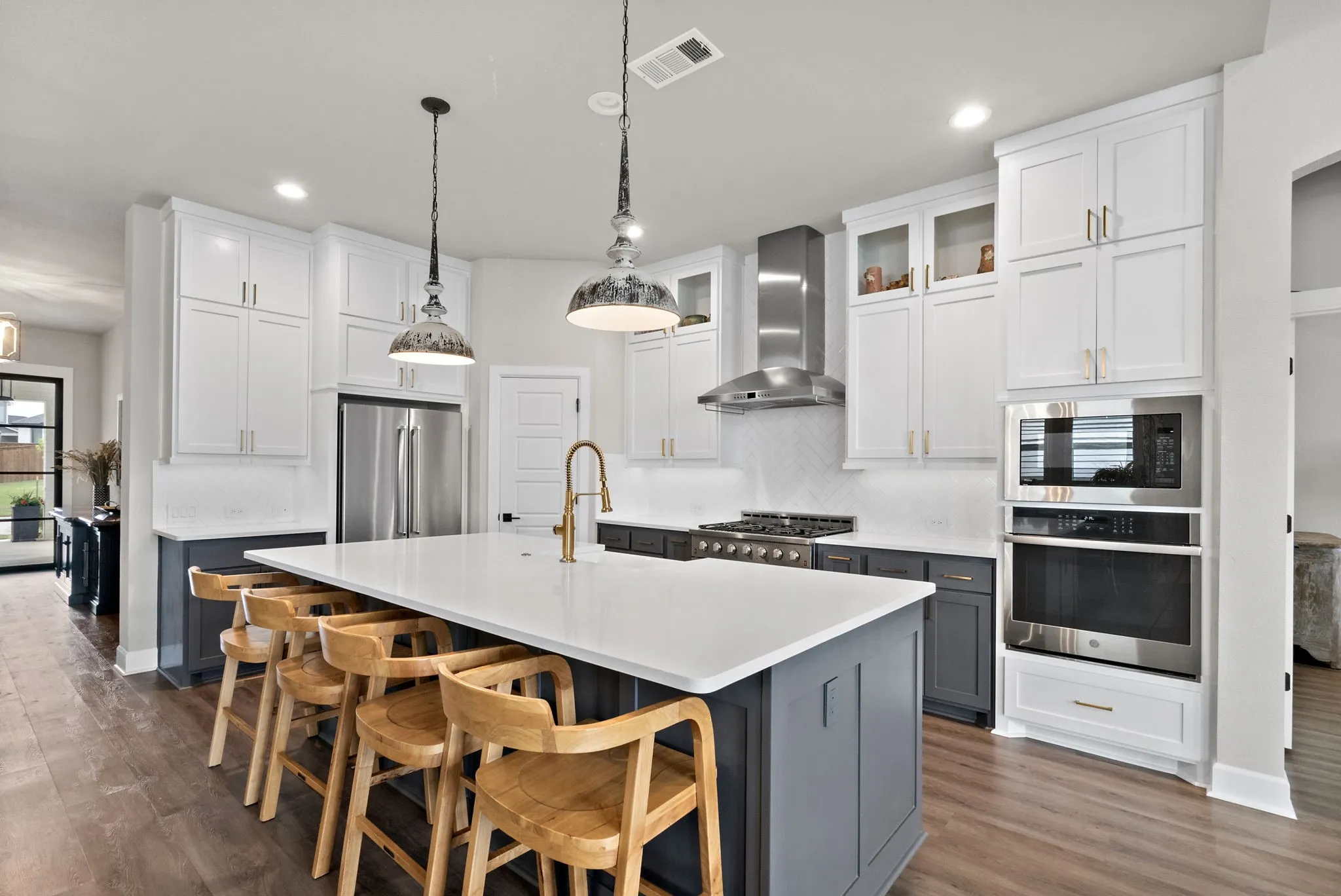 Expansive kitchen island with a solid surface countertop, wood-finish flooring, two-tone cabinetry, stainless steel appliances, and two pendant light fixtures