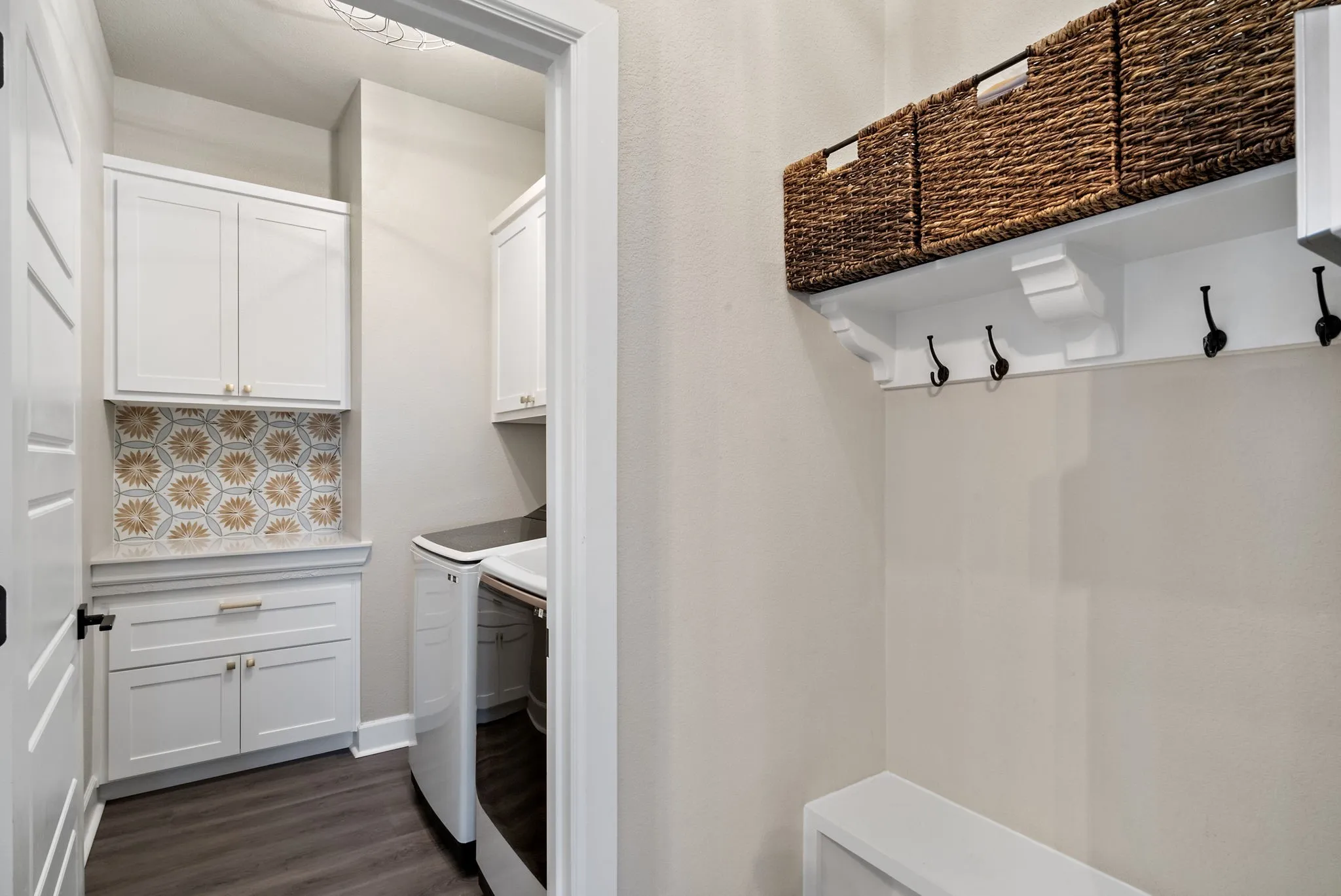 Laundry area with white cabinetry, patterned tile backsplash, and wood-finish flooring