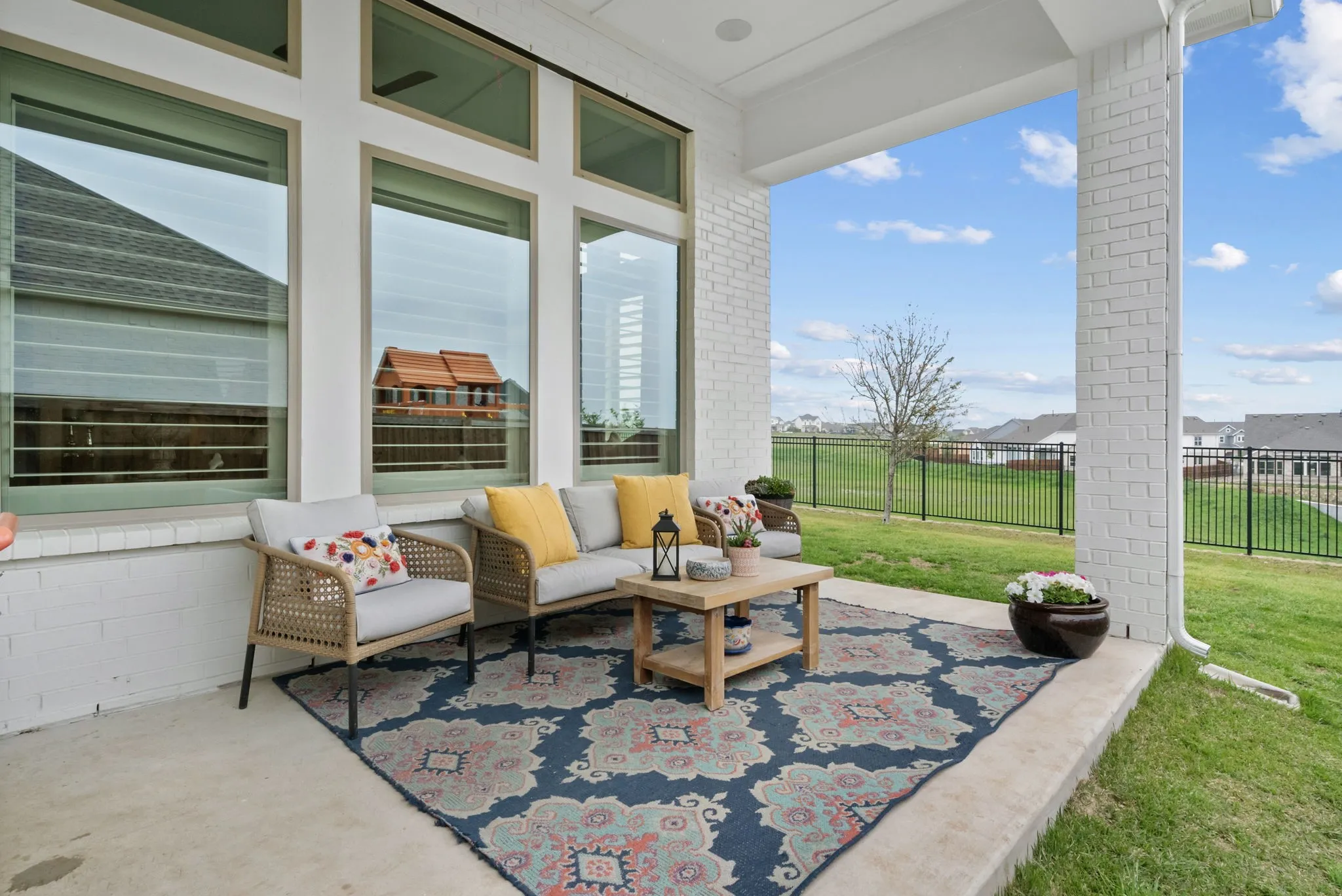 Covered patio with a concrete surface, white brick columns, and large windows