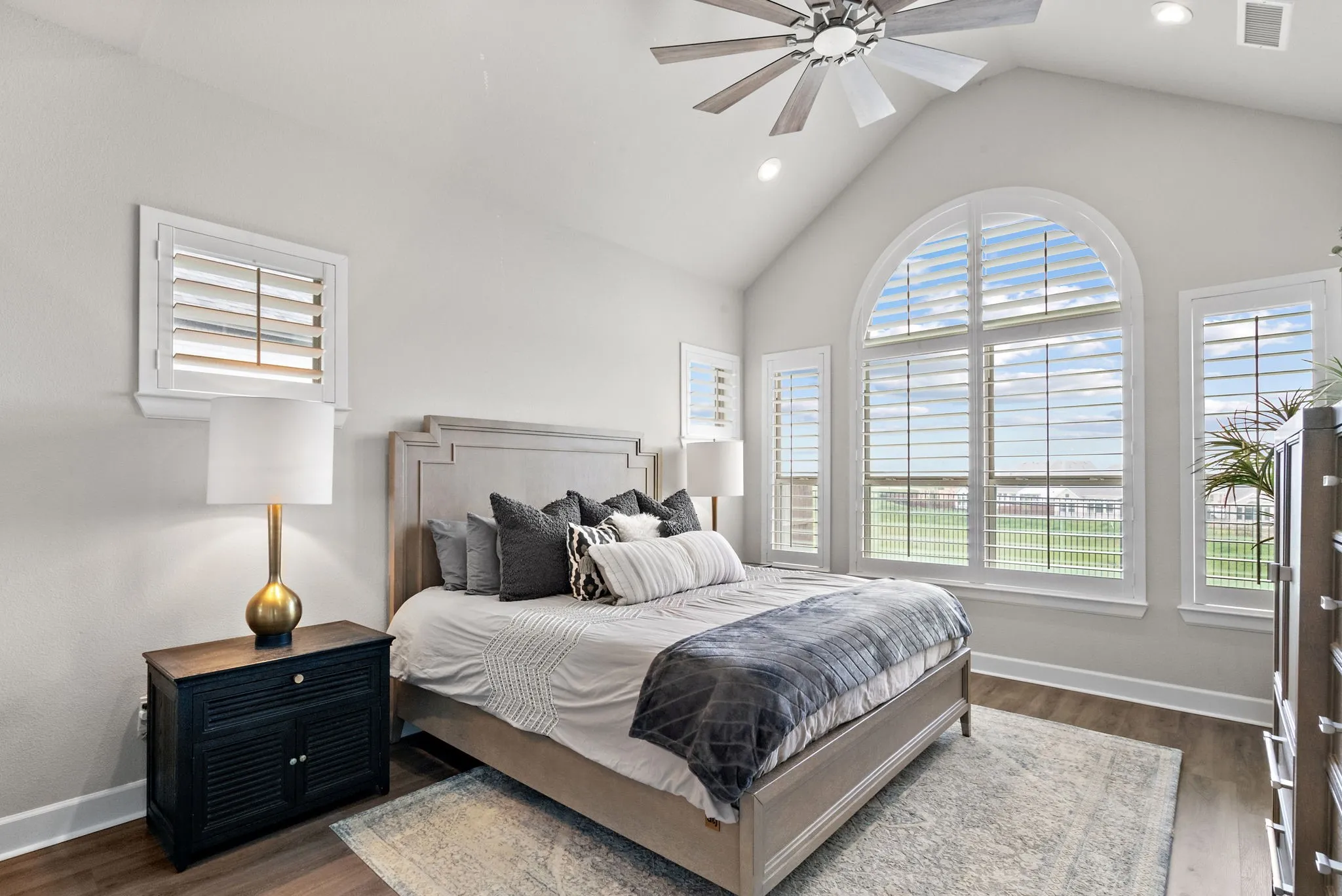 Vaulted ceilings featuring a ceiling fan, arched windows, plantation shutters, and wood-finish flooring